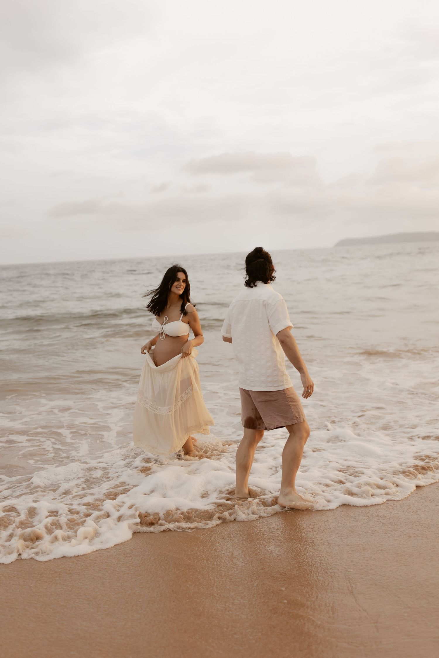 A couple playing in ocean waves at sunset on a sandy beach.