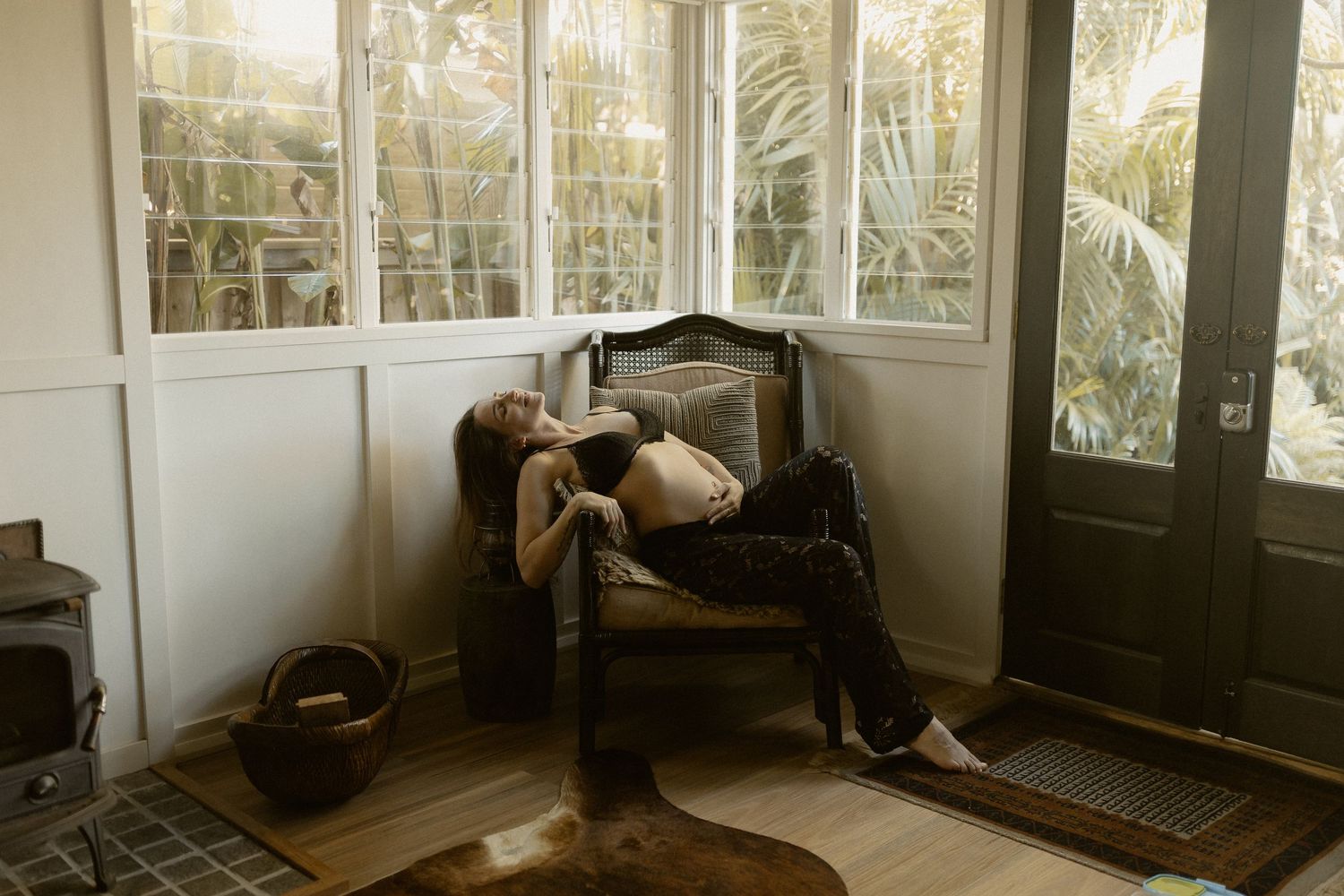 Someone relaxes in a vintage armchair by sunlit windows in a cozy corner with hardwood floors.
