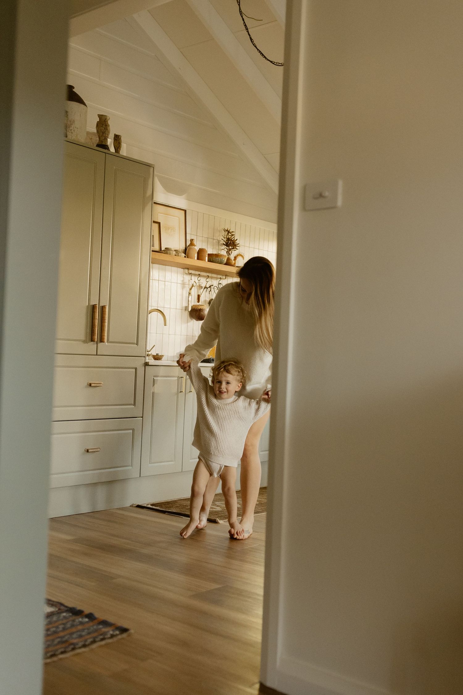 Sunlit kitchen scene through doorway showing casual morning interaction.