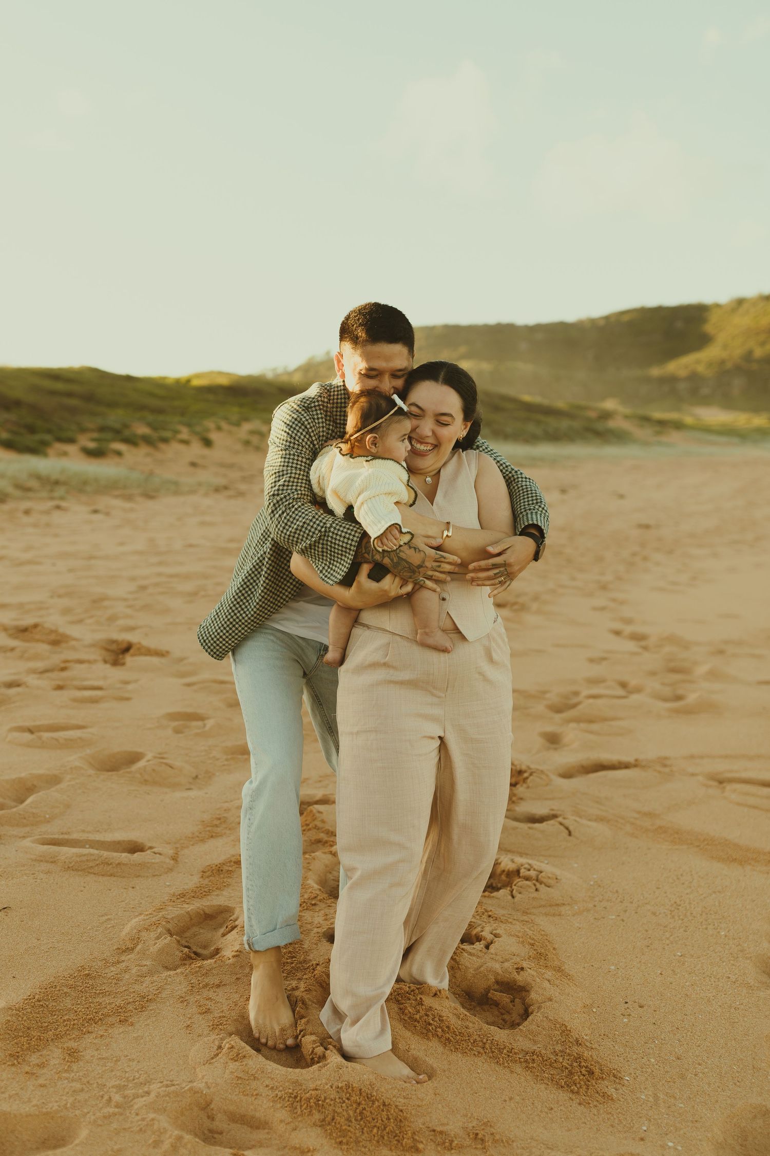 Two people in casual attire share intimate moments while dancing together on a sandy beach at sunset.