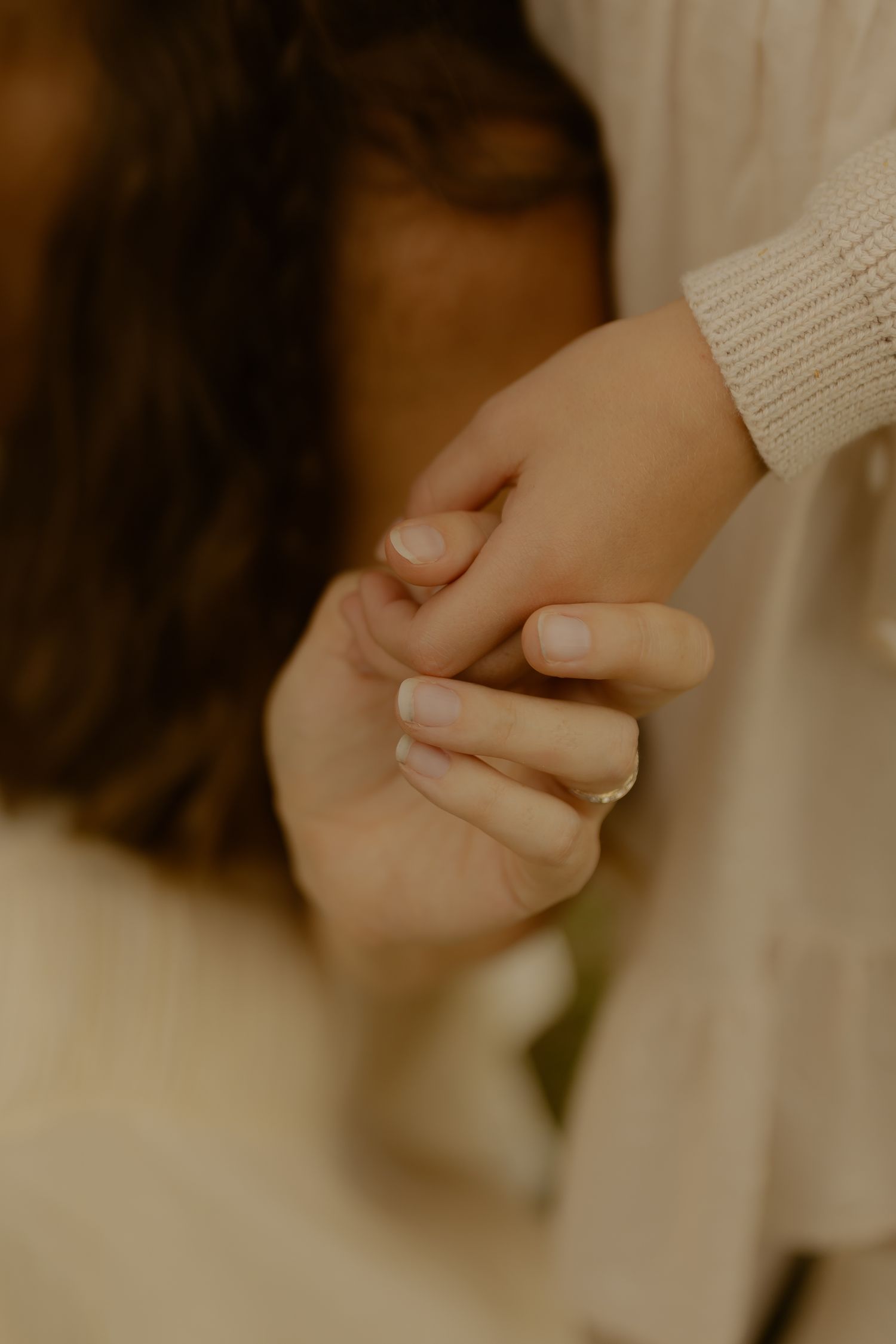 Two people gently holding hands in a warm, tender moment, wearing cream-colored sweaters.