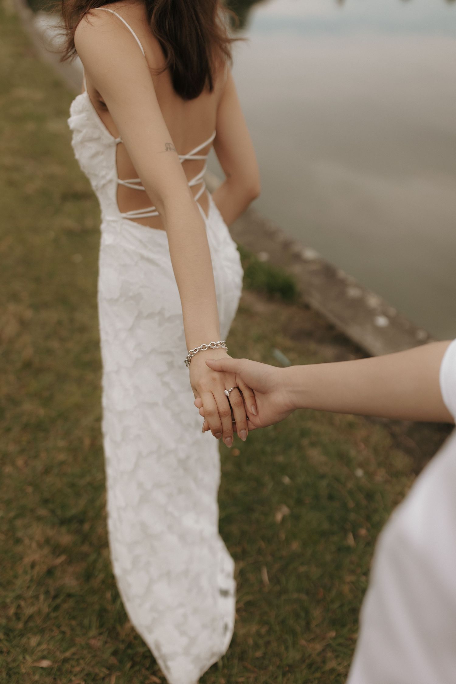 Close-up shot of hands holding together in an intimate moment, wearing white lace dress and jewelry.