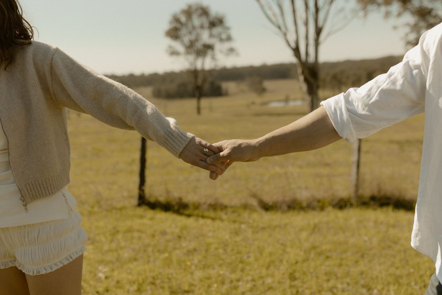 Close-up shot of two people holding hands in a sunlit field.