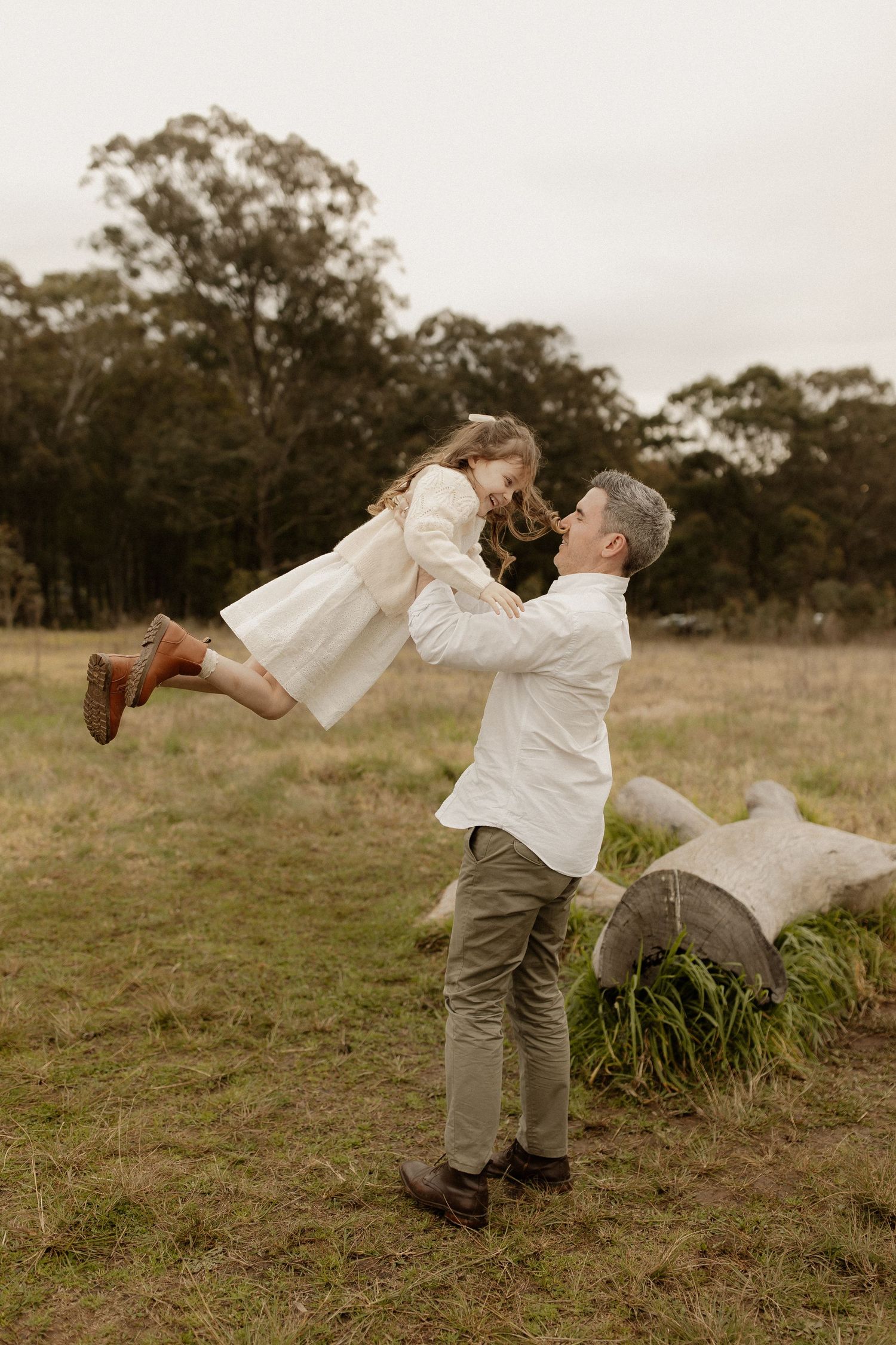 Playful couple in white outfits dance and twirl together in an open field at dusk.