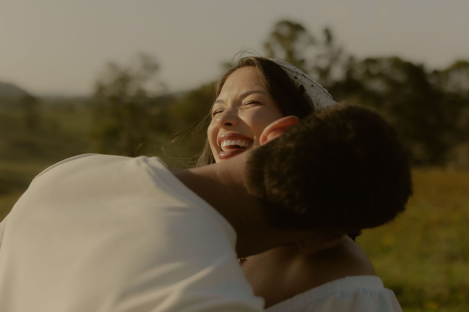 A couple embraces warmly in a golden sunlit field during sunset, sharing a joyful moment together.