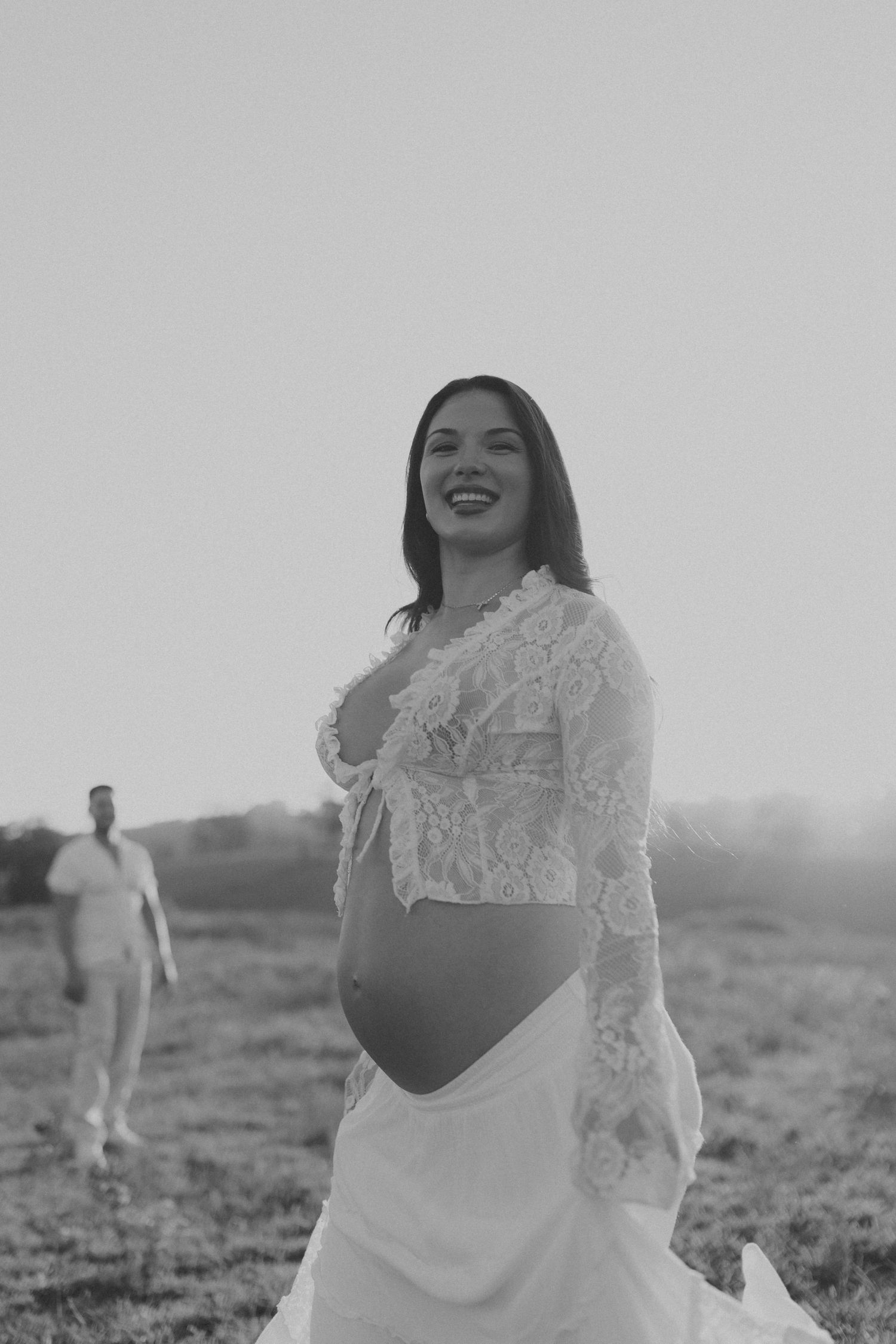 A joyful outdoor photoshoot in black and white featuring someone in a white lace dress against an open field.