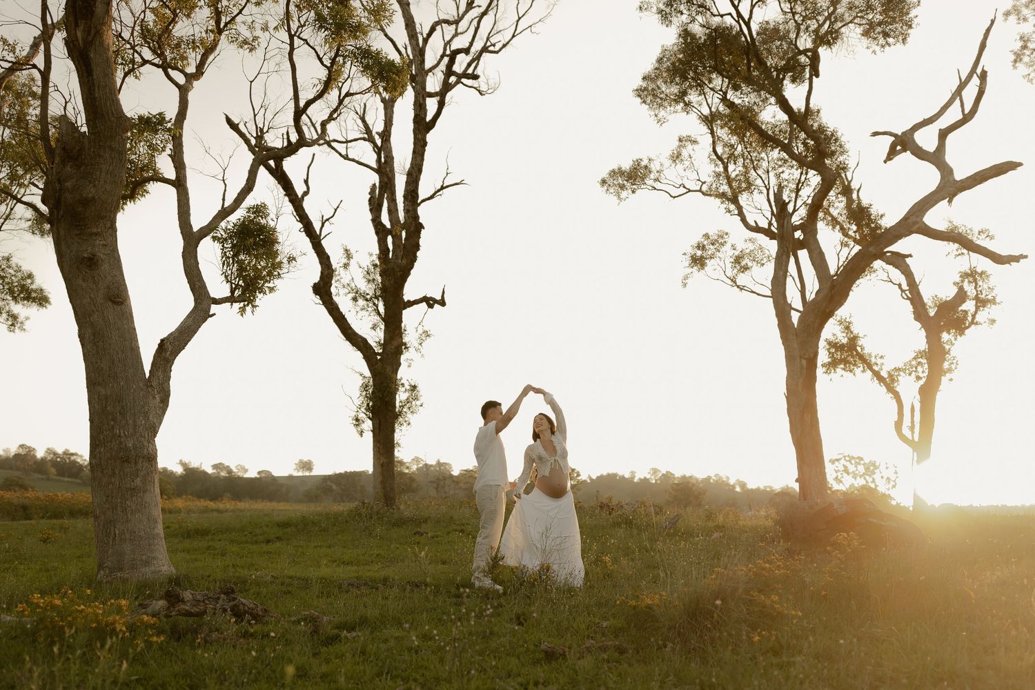 Silhouetted couple dancing among trees at sunset in romantic outdoor setting.