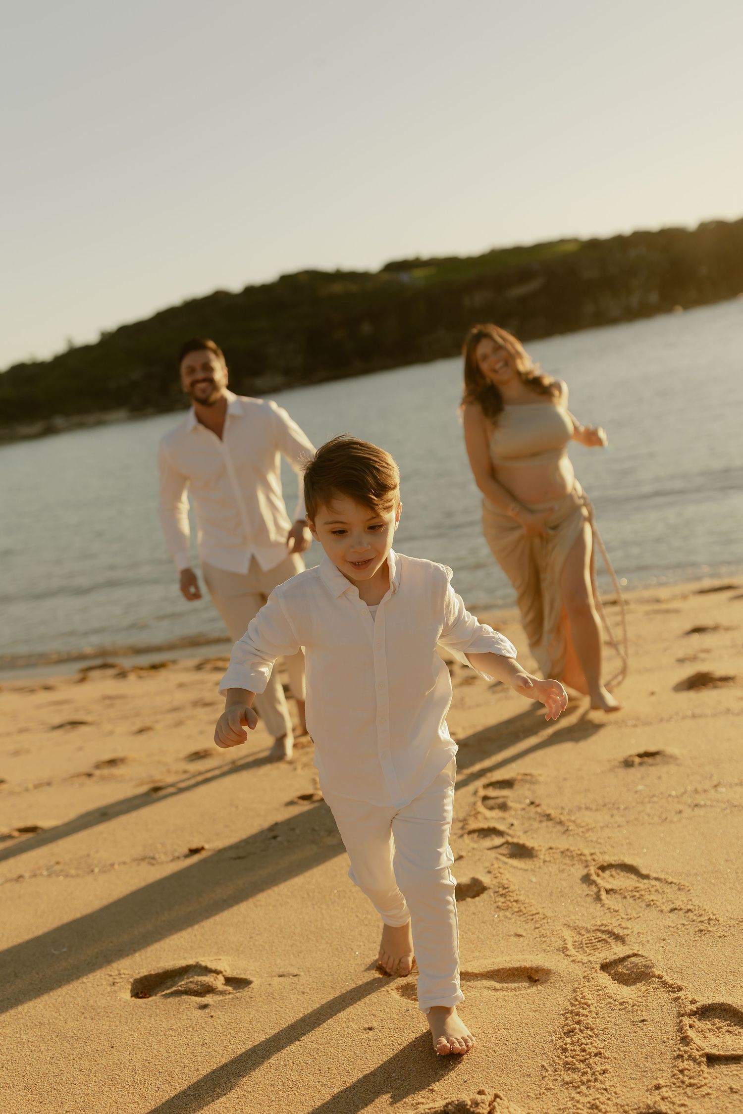 A joyful family runs on a sunny beach at golden hour, with a young boy leading his parents along the shoreline.