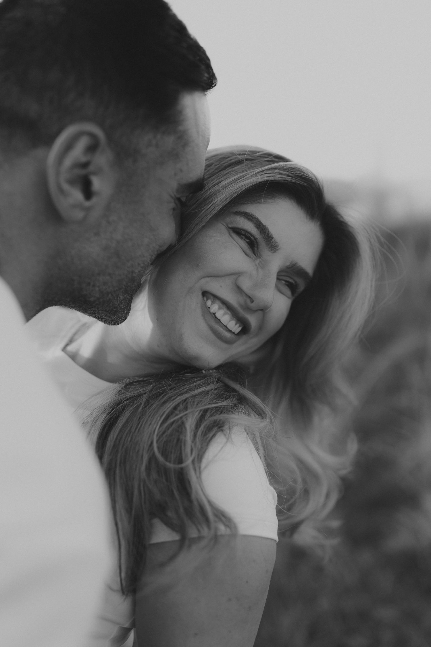 Black and white photo of smiling couple sharing a tender romantic moment outdoors.