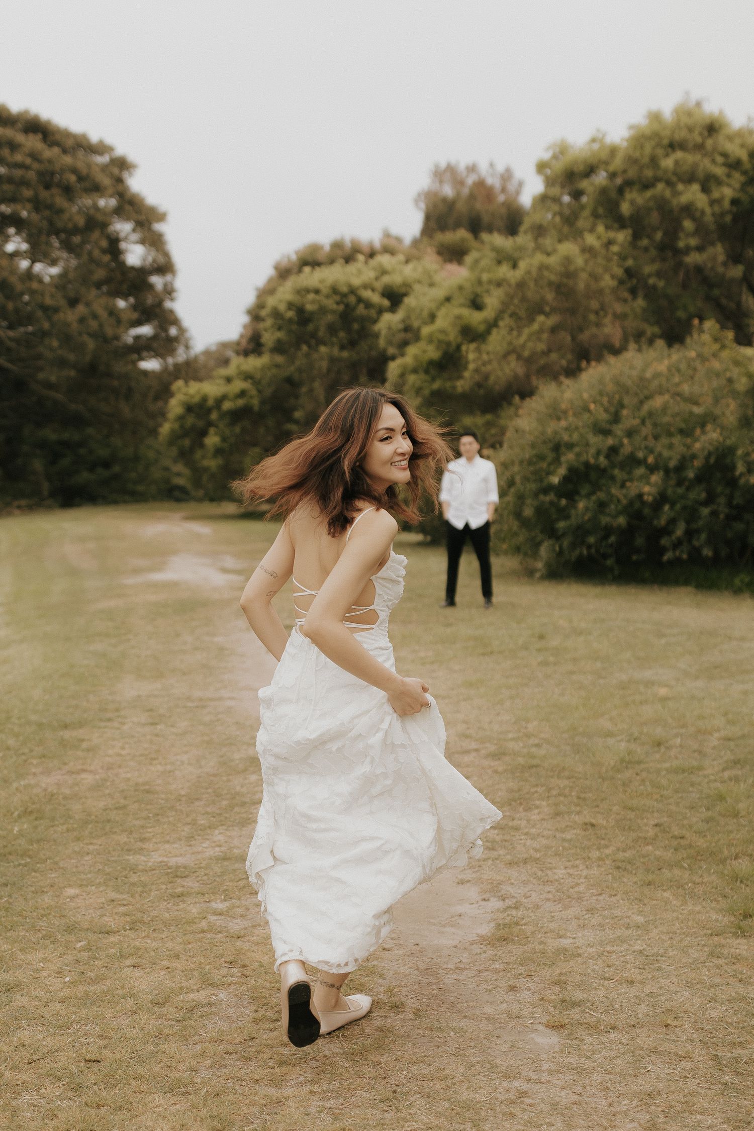 A person in a flowing white wedding dress twirls gracefully in a grassy outdoor setting.