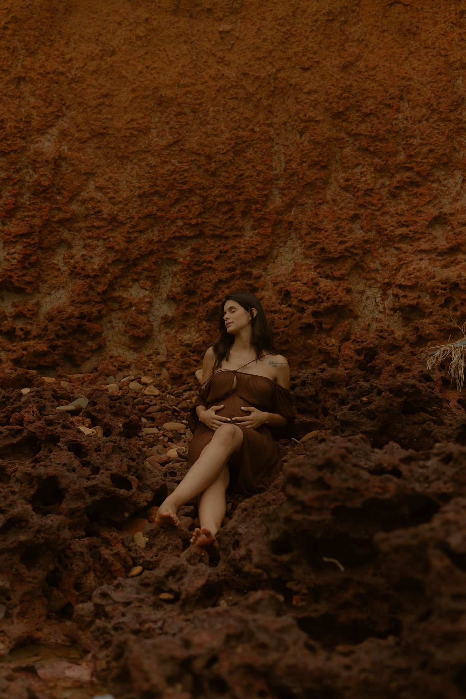 A person in dark attire reclines against a textured rustic wall in sepia tones.