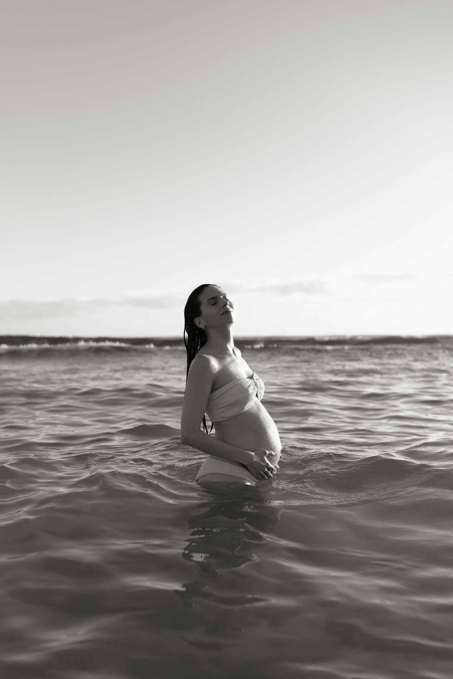 A series of black and white photos showing someone floating and arching back in ocean waves against a distant horizon.