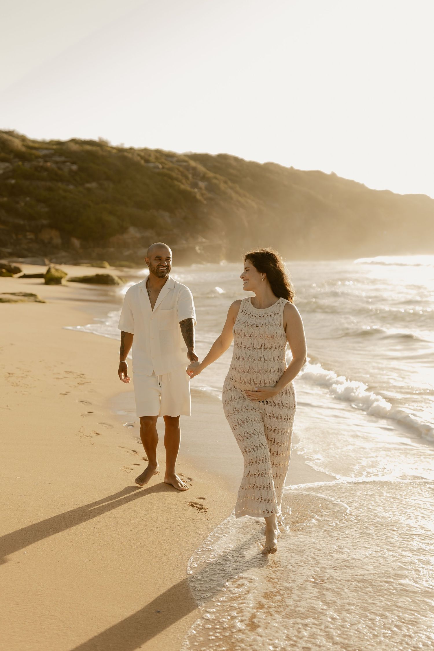 A couple walks hand in hand along the shoreline during sunset at the beach.