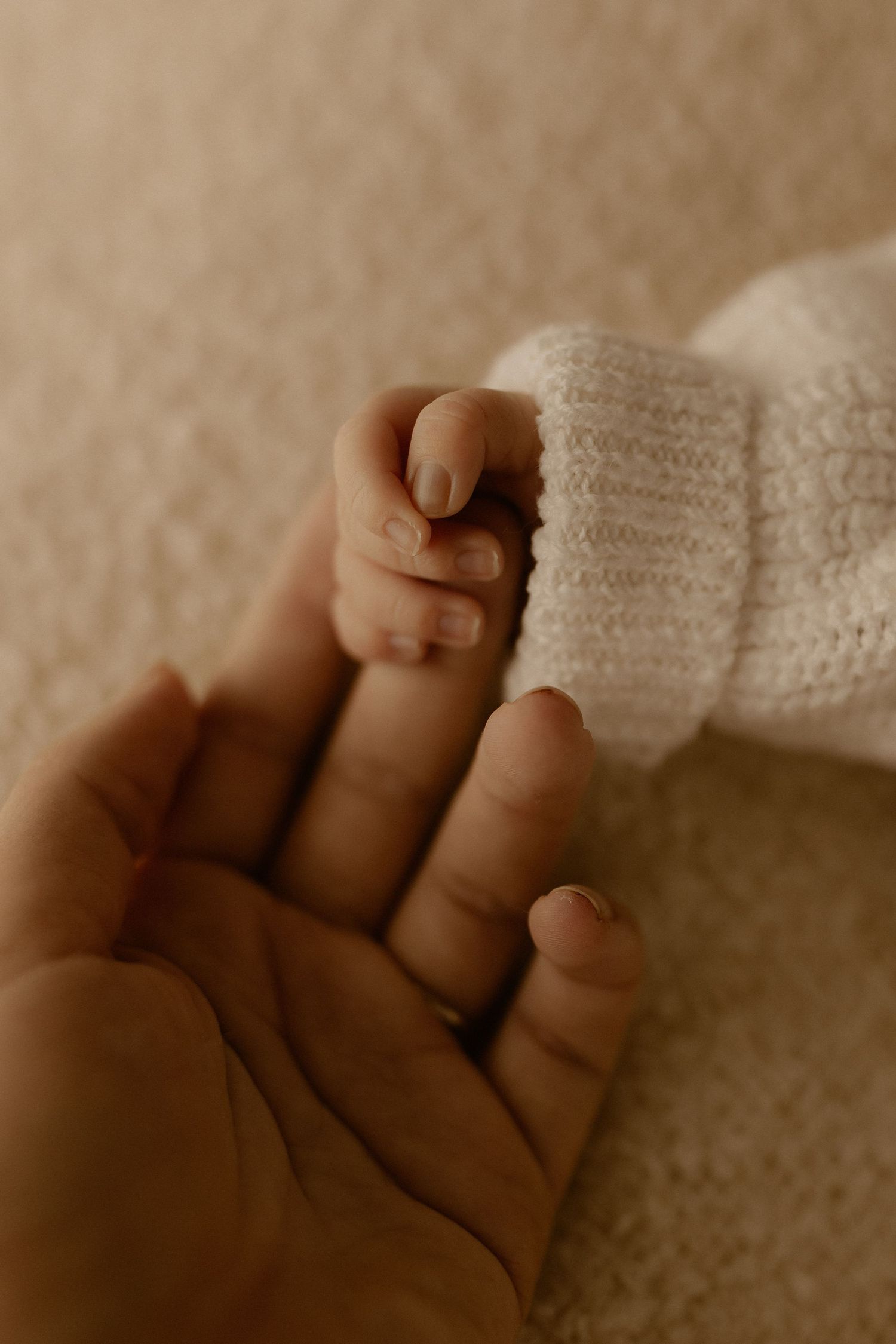 Close-up sequence of tiny baby fingers grasping against a soft knitted white fabric background.