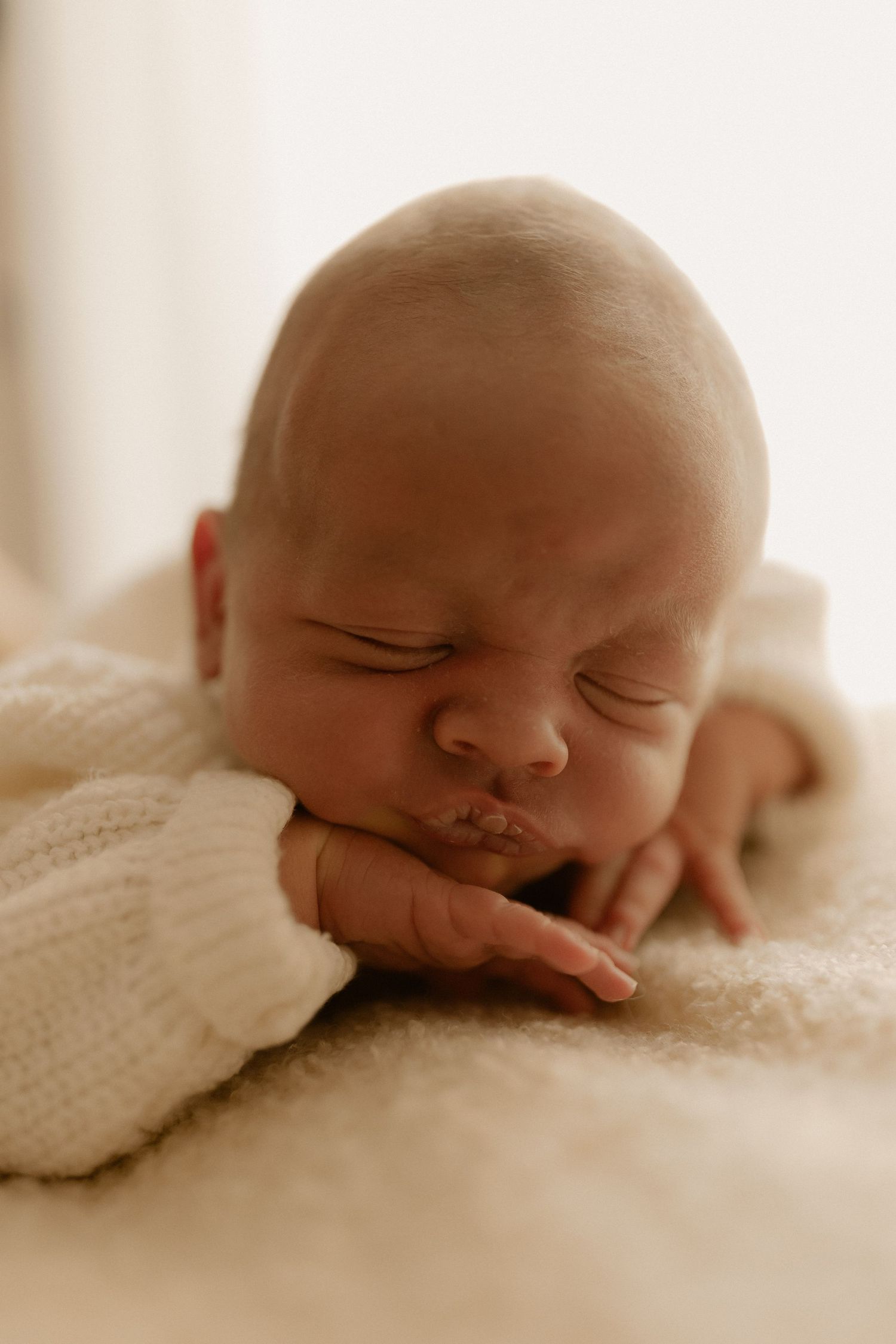 Peaceful sleeping newborn baby resting on soft white blanket in warm sepia tones.