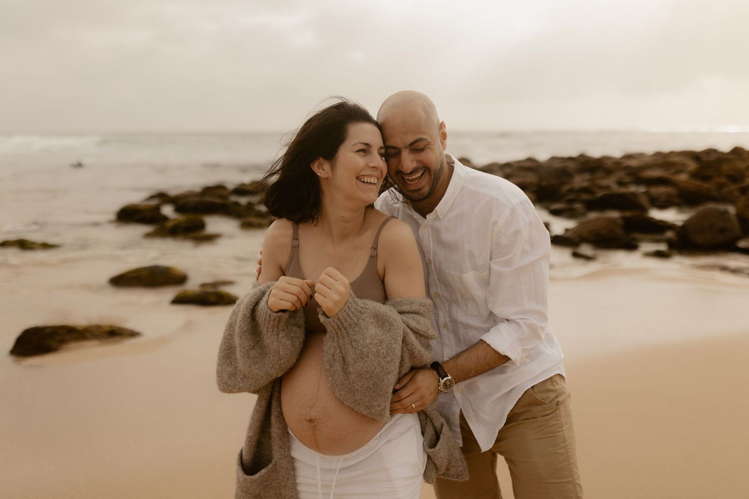 A couple shares romantic moments on a sandy beach during sunset, creating intimate and joyful candid photographs.