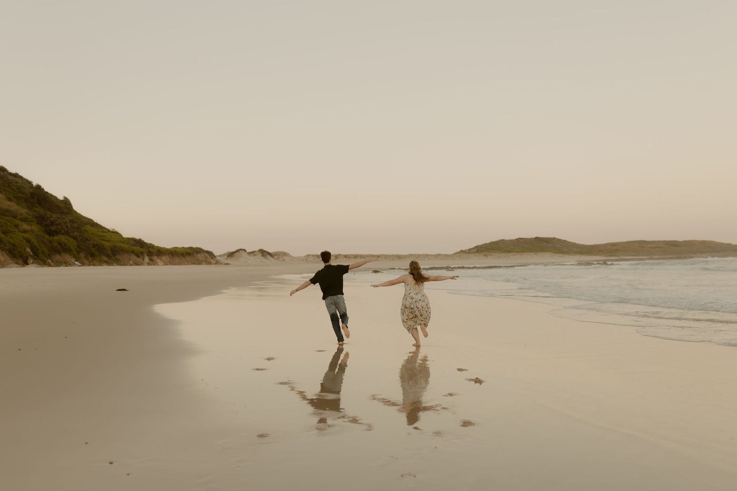 Two silhouetted figures dance and play on a serene beach at golden hour.