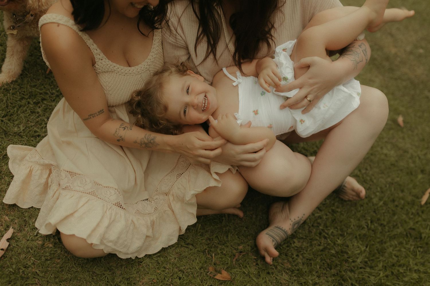 Intimate family portrait session on grass with flowing cream-colored dresses and natural styling.
