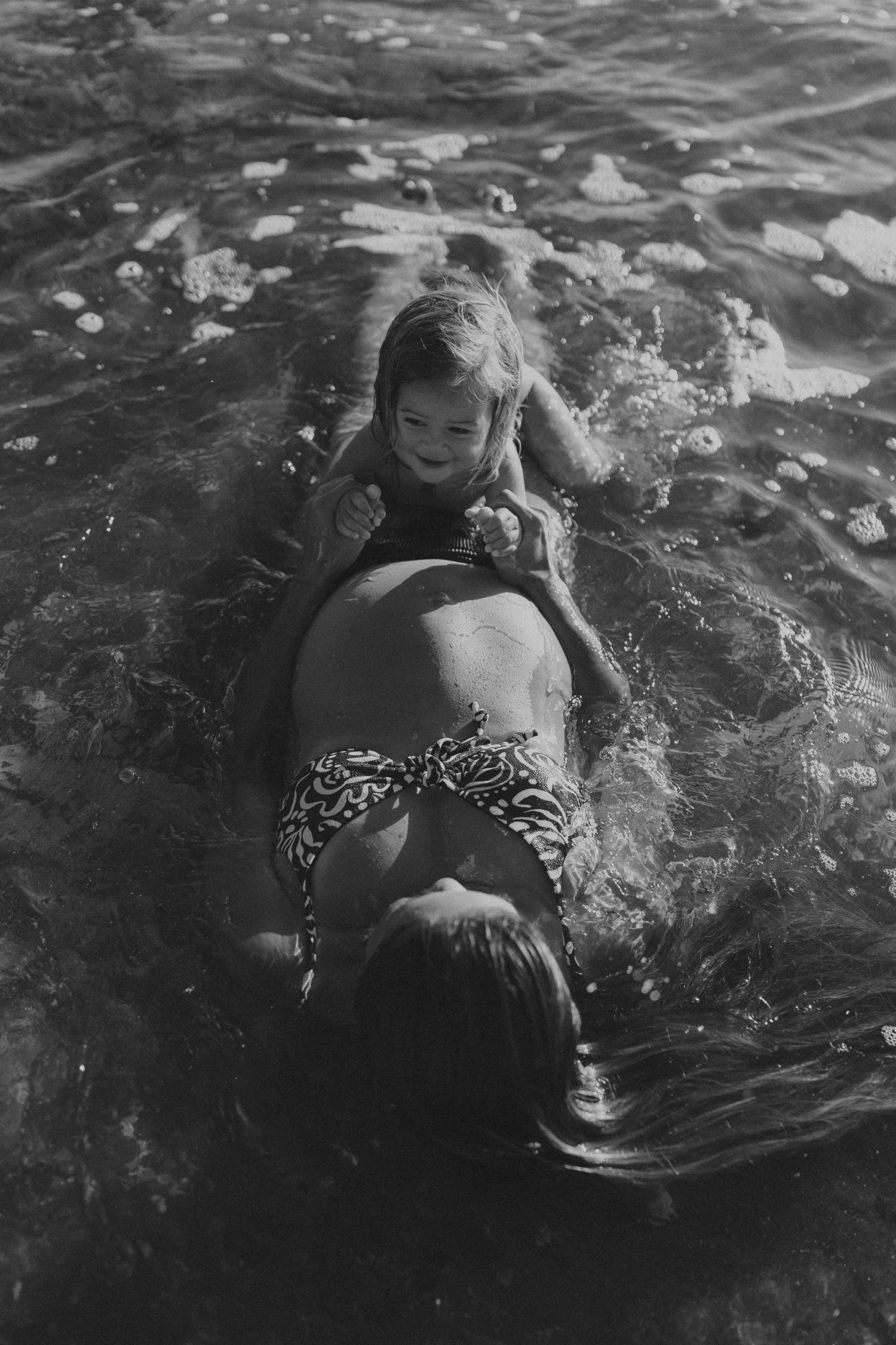 Two people floating together in rippling ocean water captured in black and white.