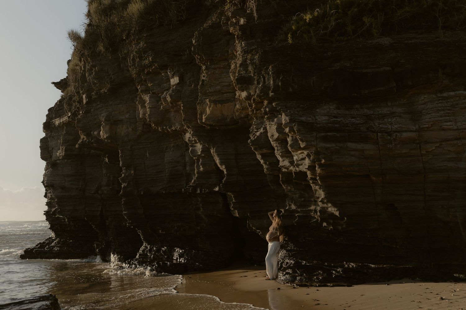 Rocky coastal cliffs and beach landscape at sunset with dramatic natural lighting and ocean waves.