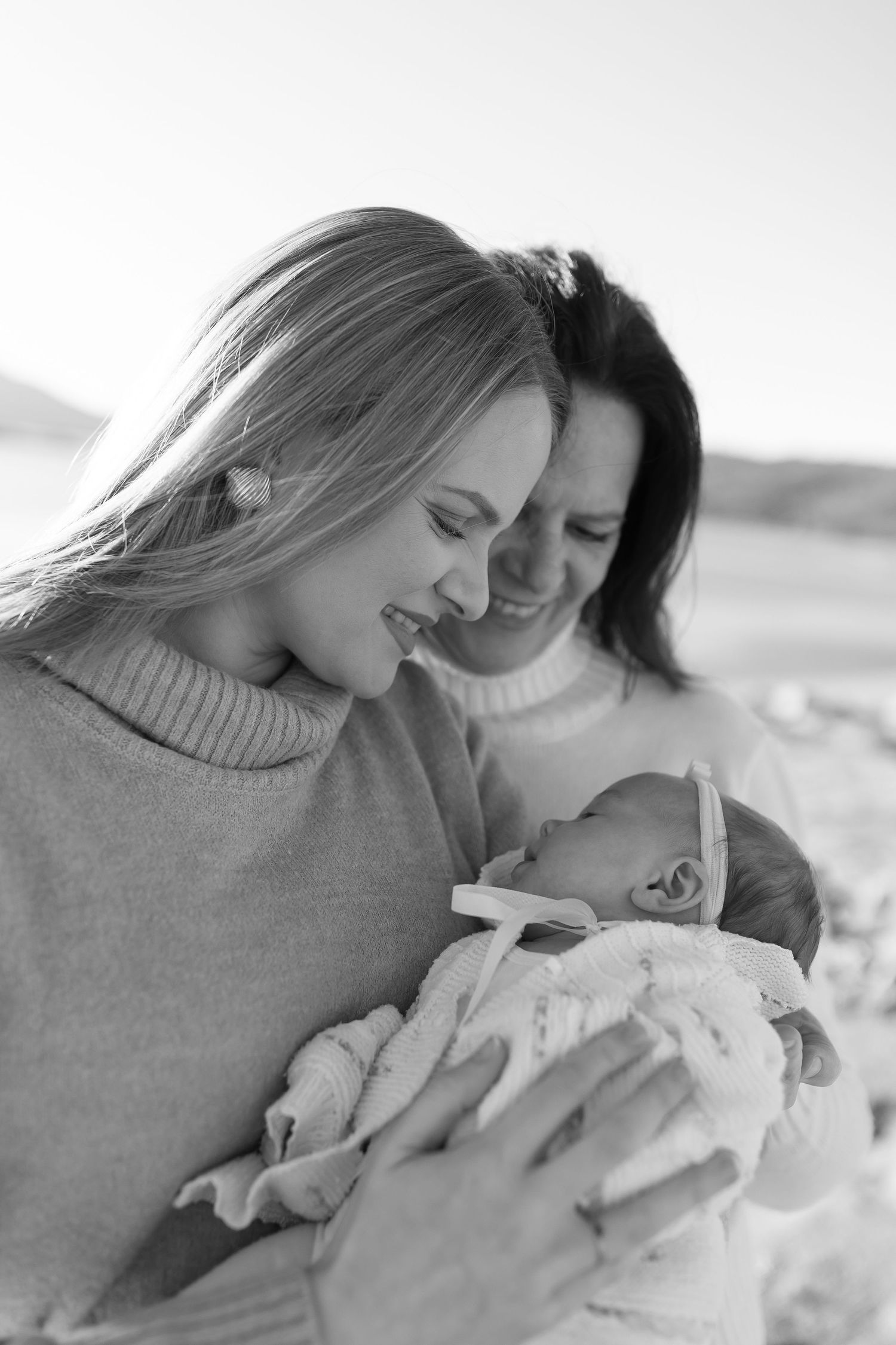 A touching black and white portrait of two people sharing a tender moment with a newborn baby wrapped in blankets.