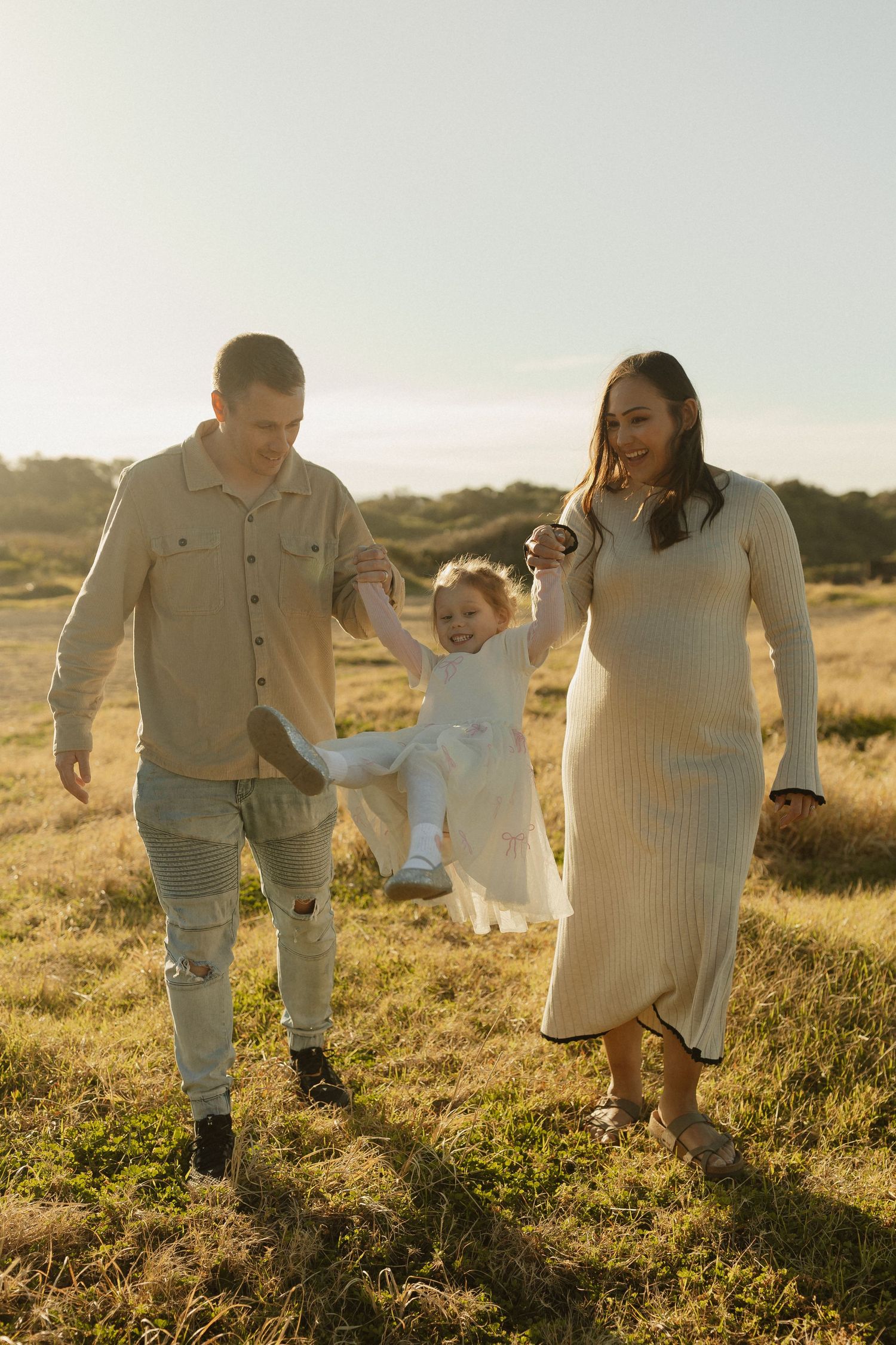 Family walks together through sun-lit field holding hands with small child.