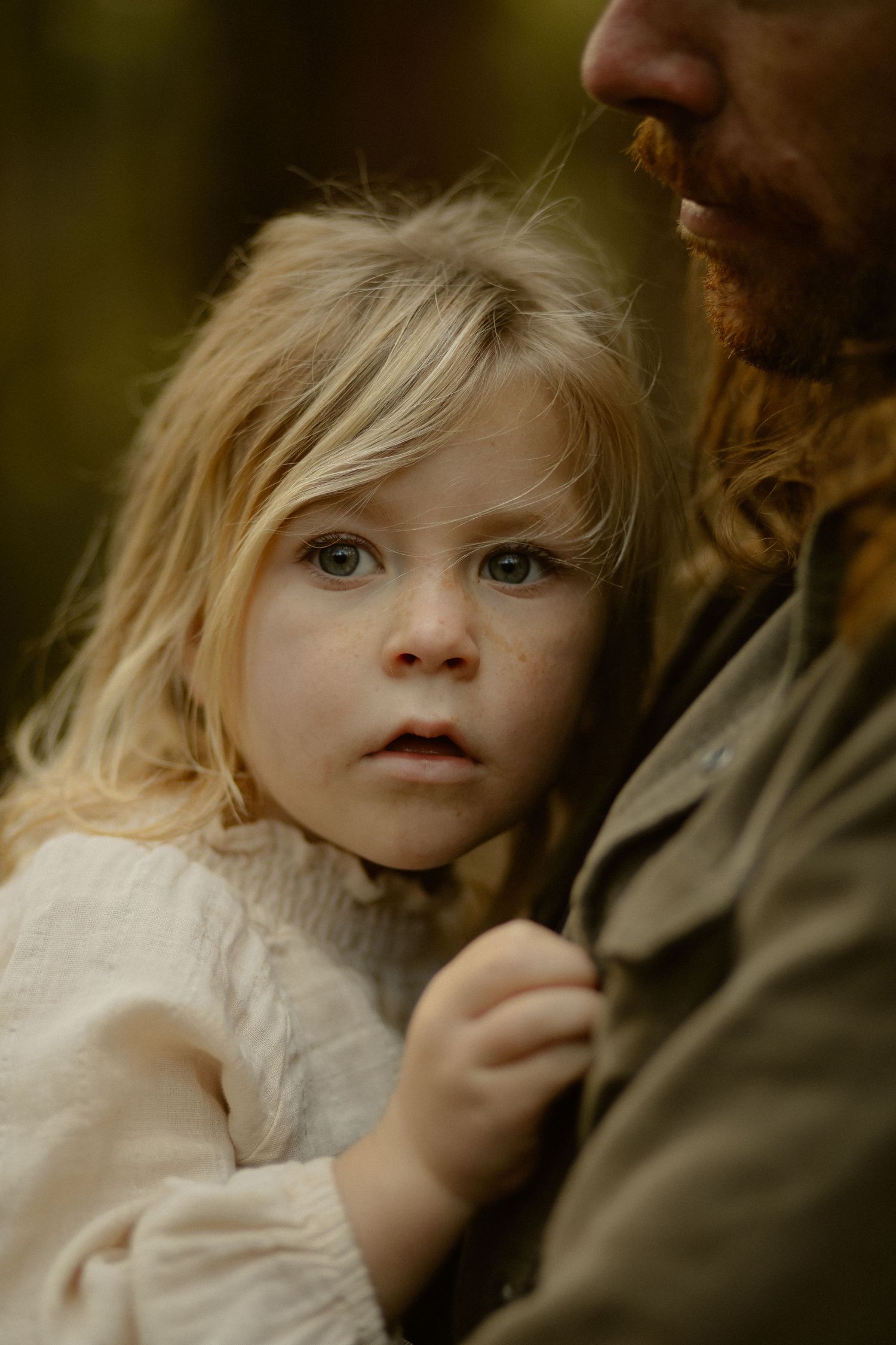 A close-up portrait shows a young child with blonde hair next to someone wearing brown clothing in soft lighting.