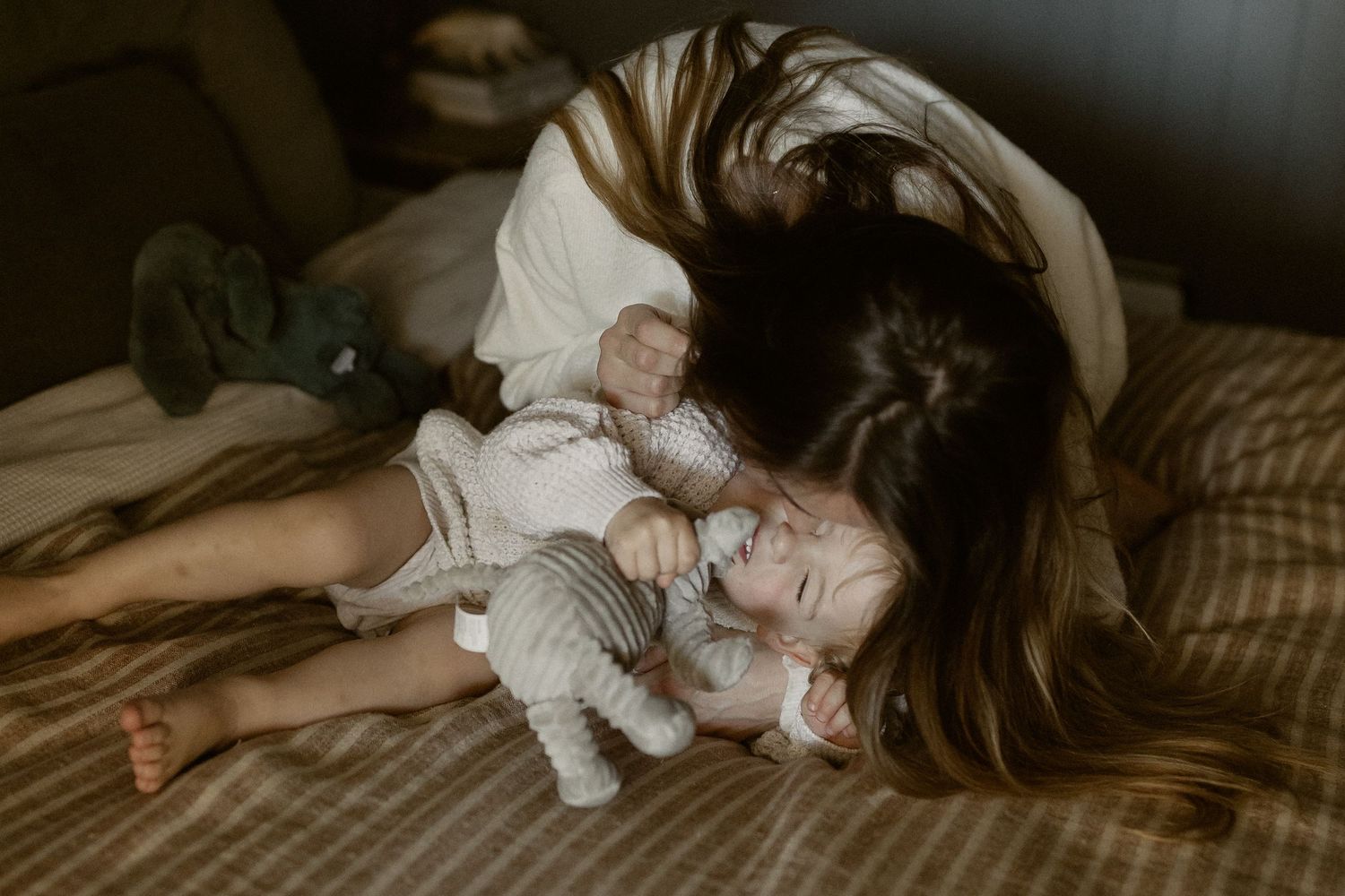 A tender moment between a parent and child cuddling together on a cozy bed in natural light.