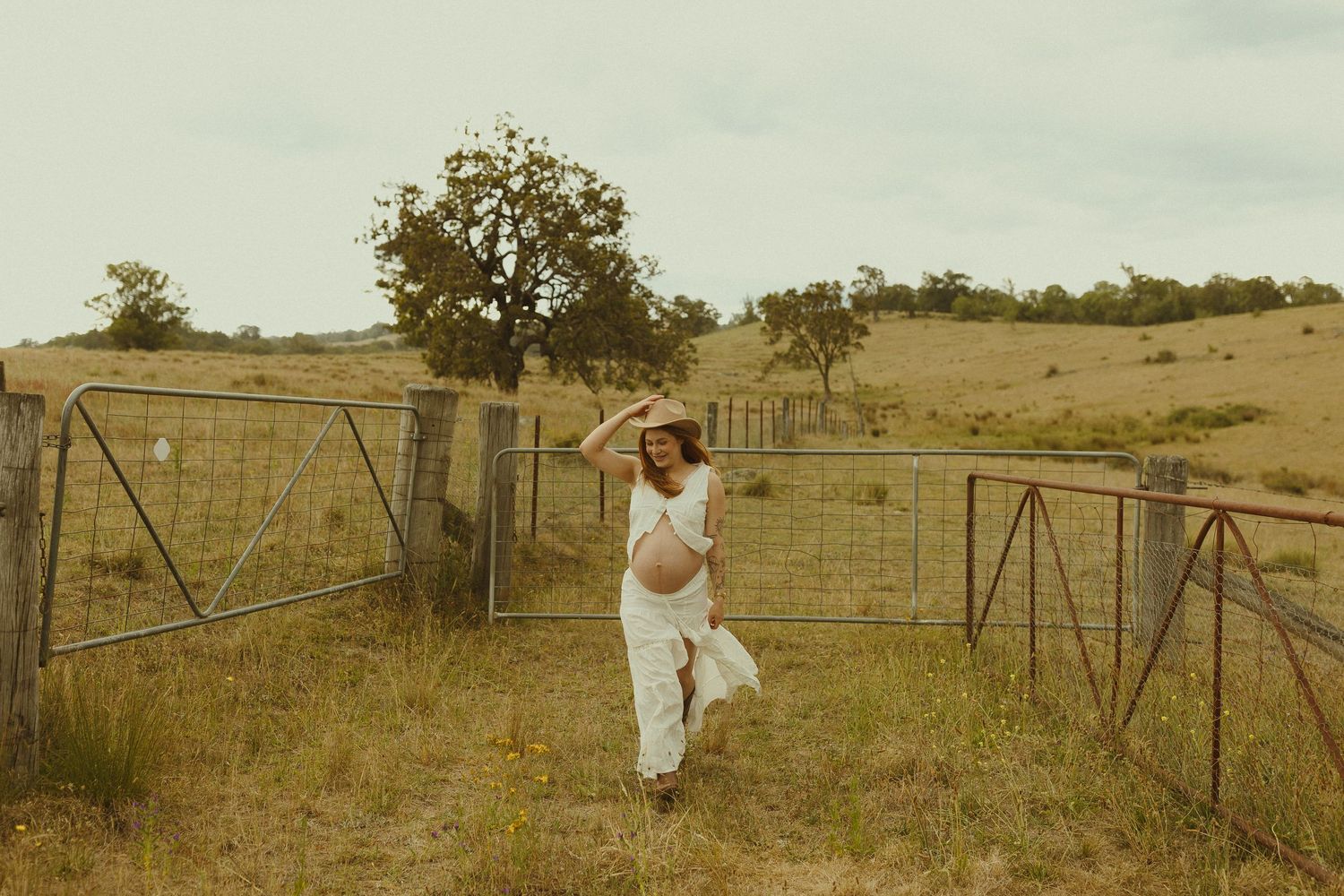 A vintage-toned photo of someone walking along a rustic fence line in a rural setting.
