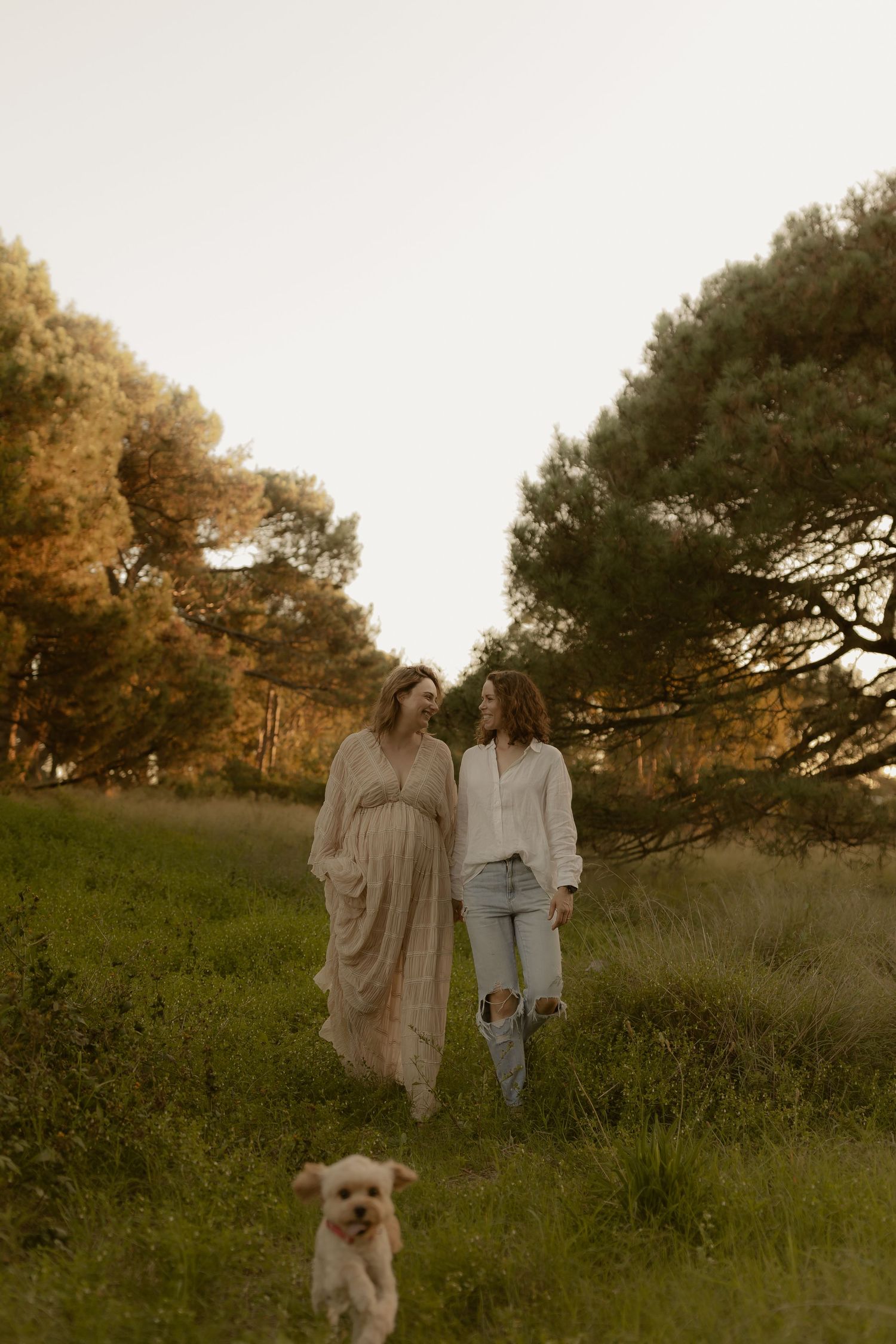 Family photoshoot in a grassy field with flowing dresses and a small fluffy dog.