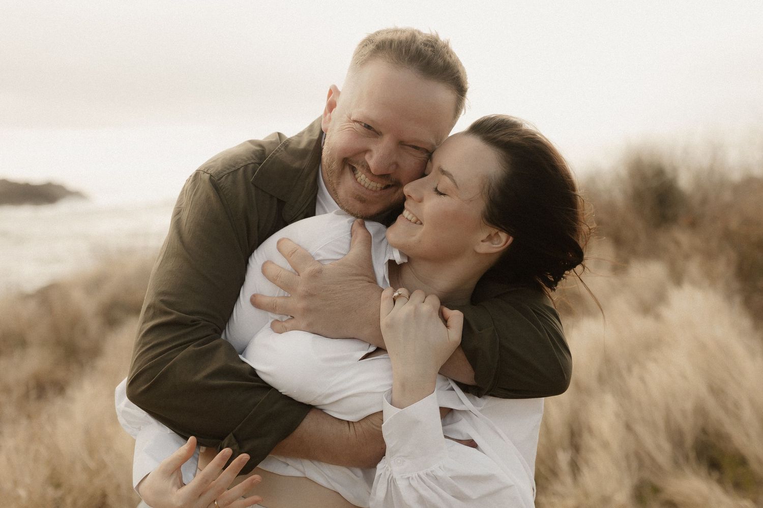A romantic couple embraces in a golden field during sunset, creating an intimate and joyful moment.