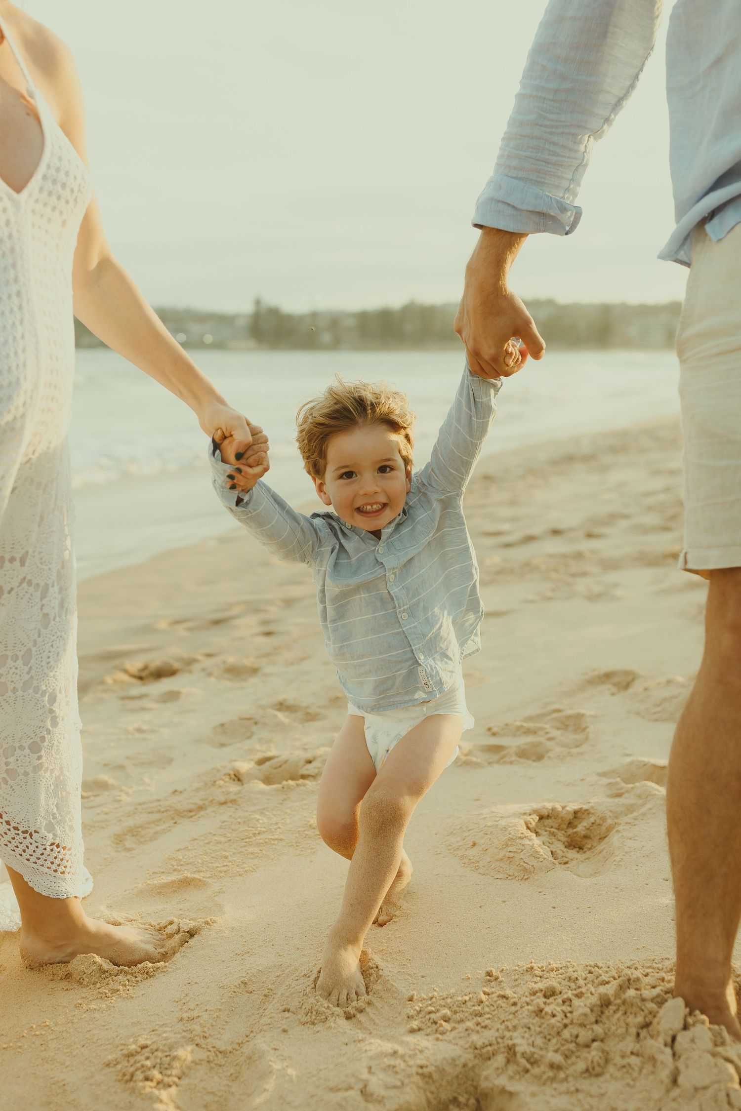 Family playing and running barefoot together on sandy beach at sunset.
