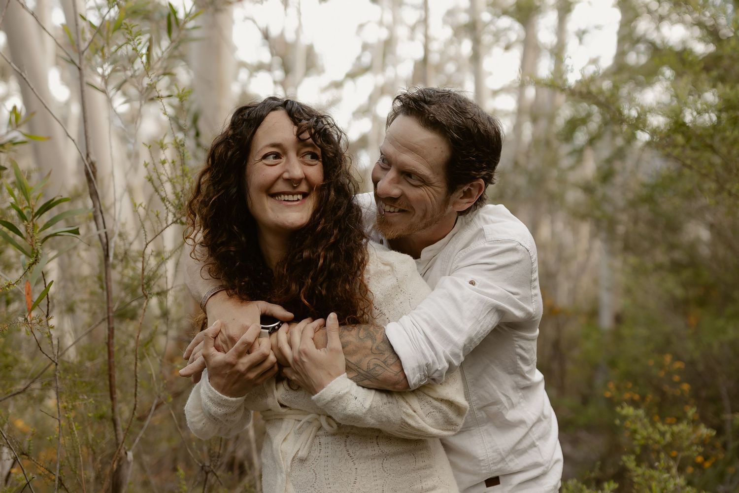 A romantic moment captured between a couple laughing together in a wooded area.