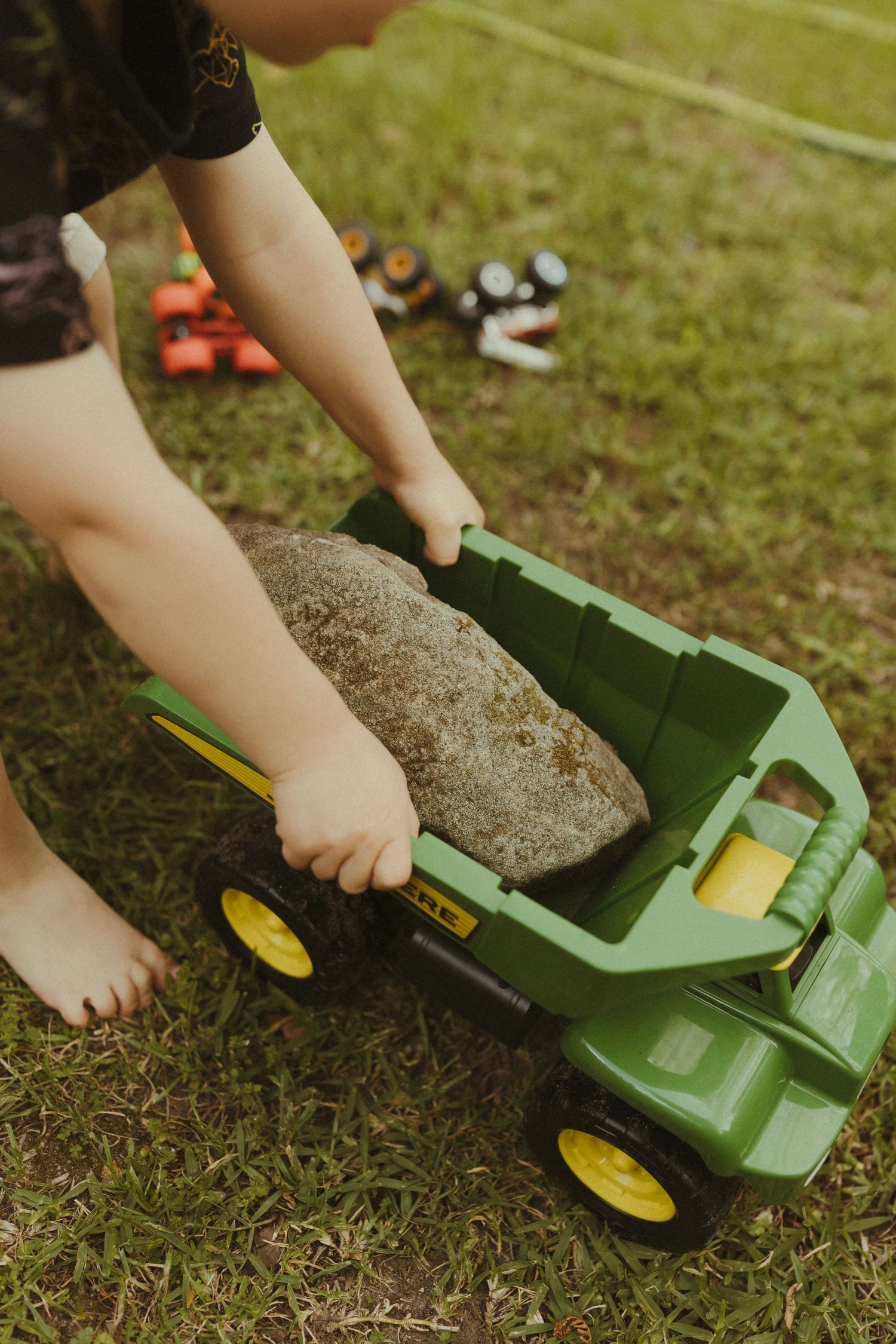 Close-up shots of hands playing with a green toy tractor on grass.