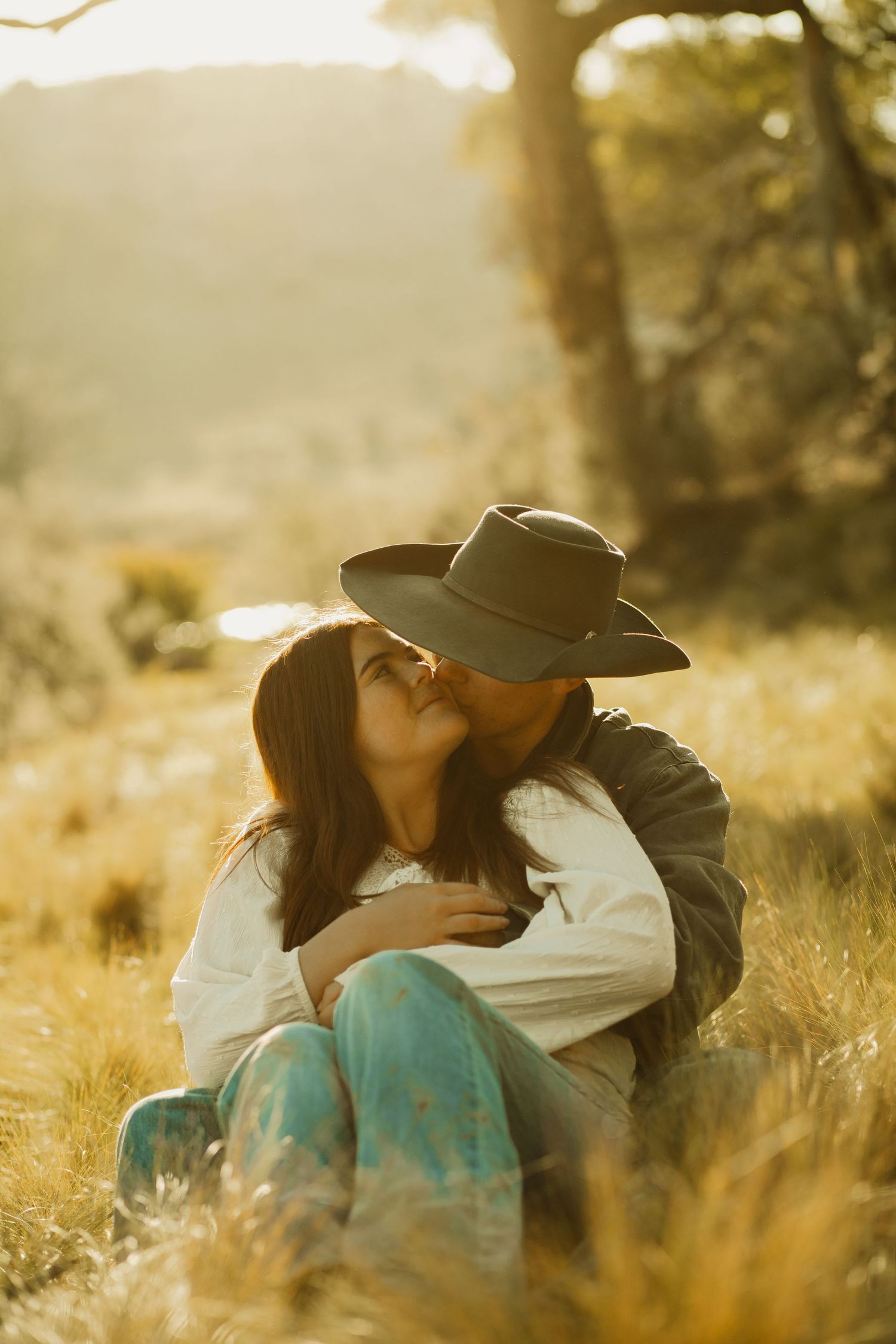 A tender embrace captured in golden hour light amidst tall grass and trees.