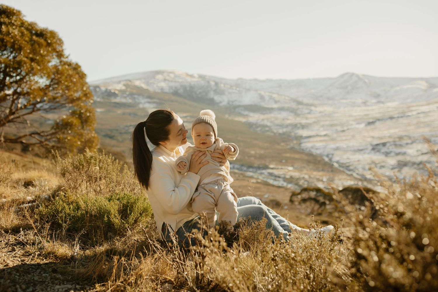 A parent and child share an intimate moment while sitting in autumn grass with mountain views in the background.