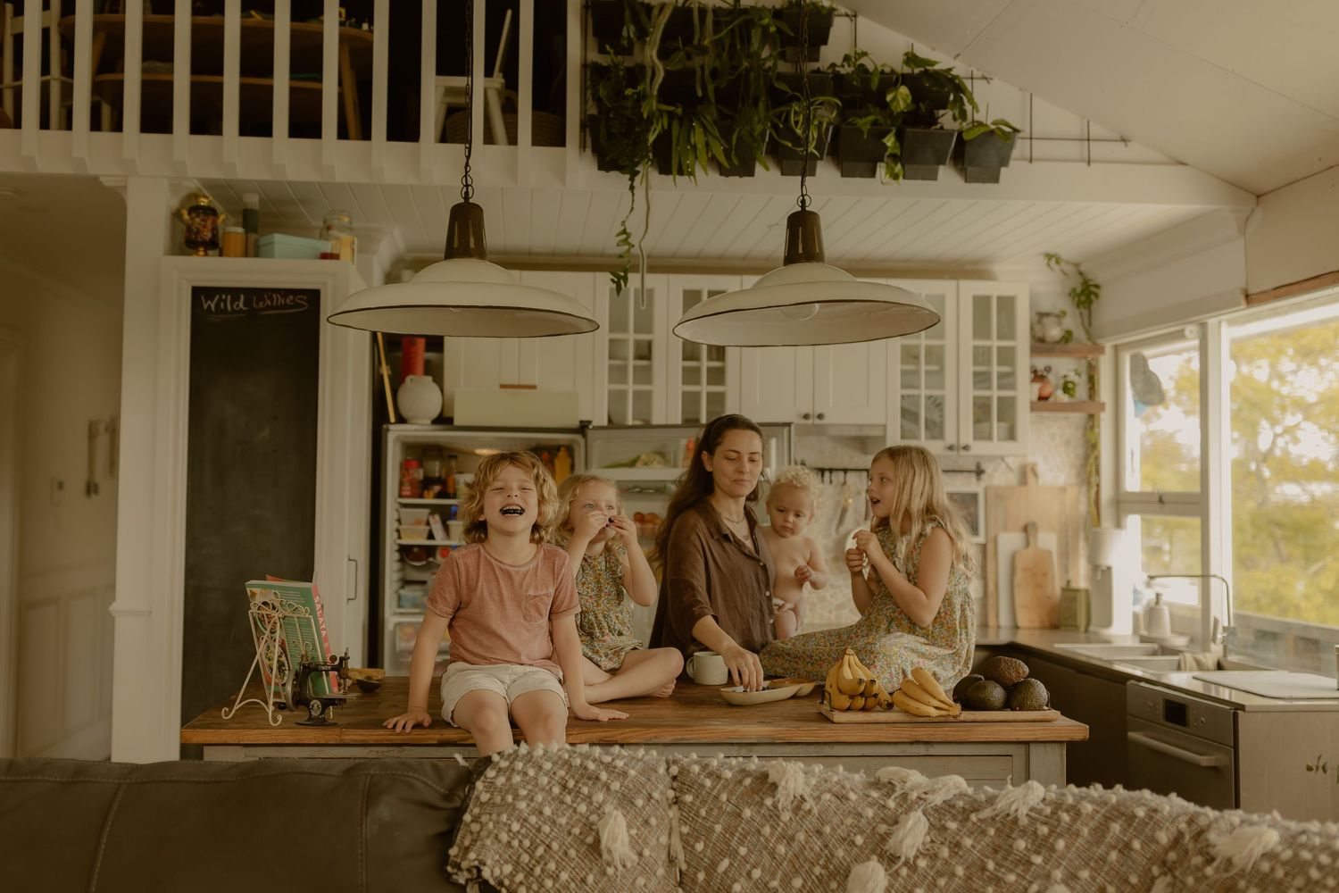 A joyful family gathers in a cozy kitchen, with children laughing and a mother holding a baby near a wooden counter.