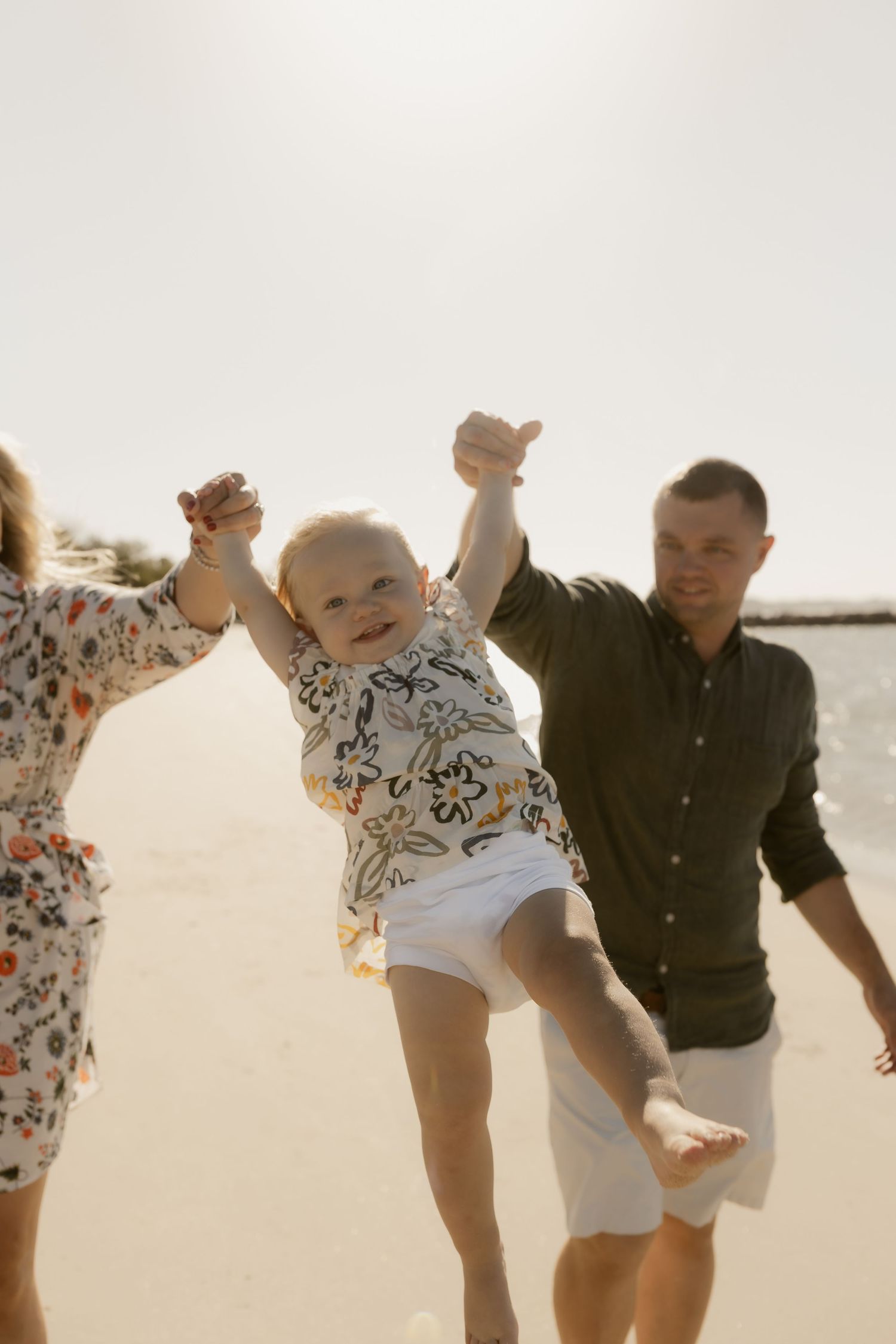 Family playing and jumping together on beach during golden hour.