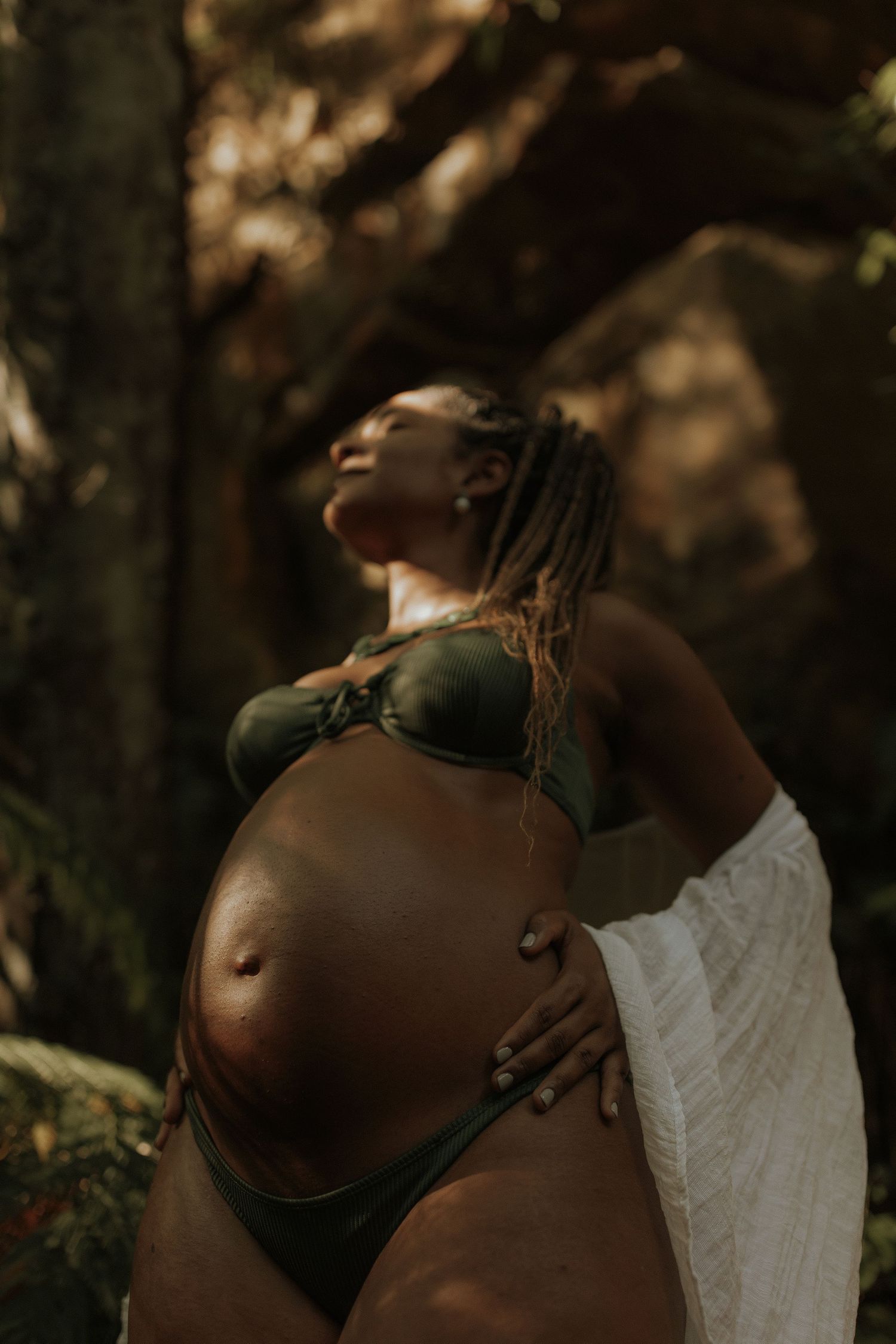 A series of intimate maternity photos showing a pregnant belly in natural lighting against a dark forest backdrop.