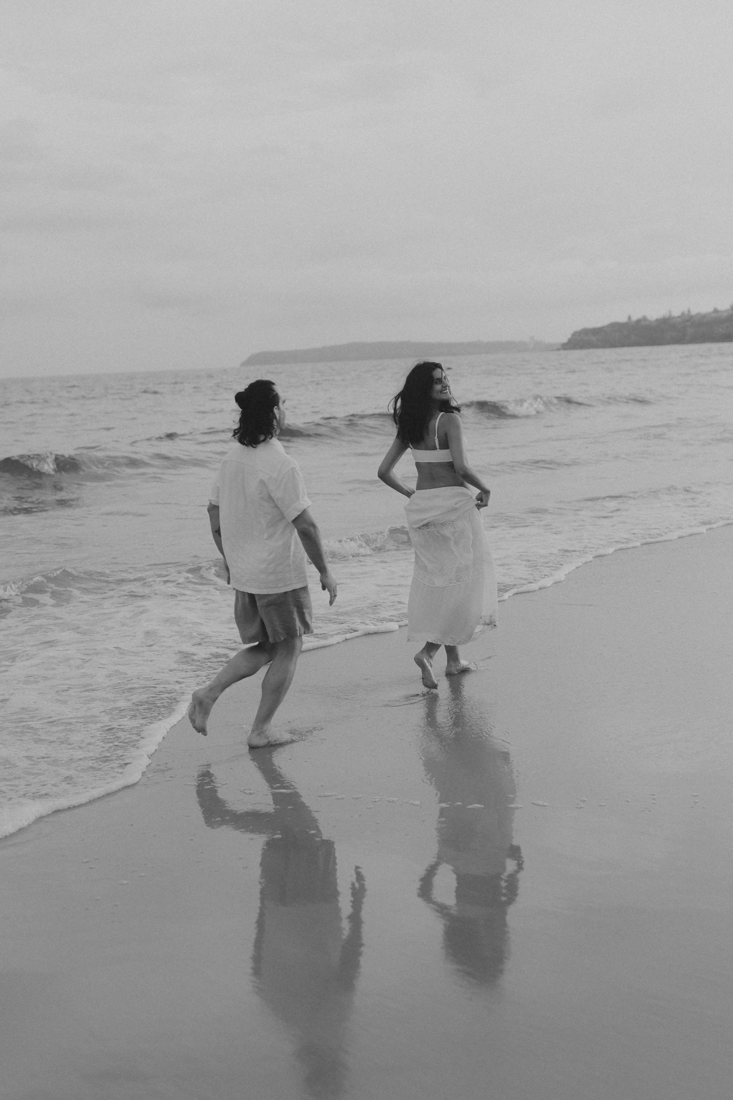 Black and white photo of figures playing and running along a misty beach shoreline.