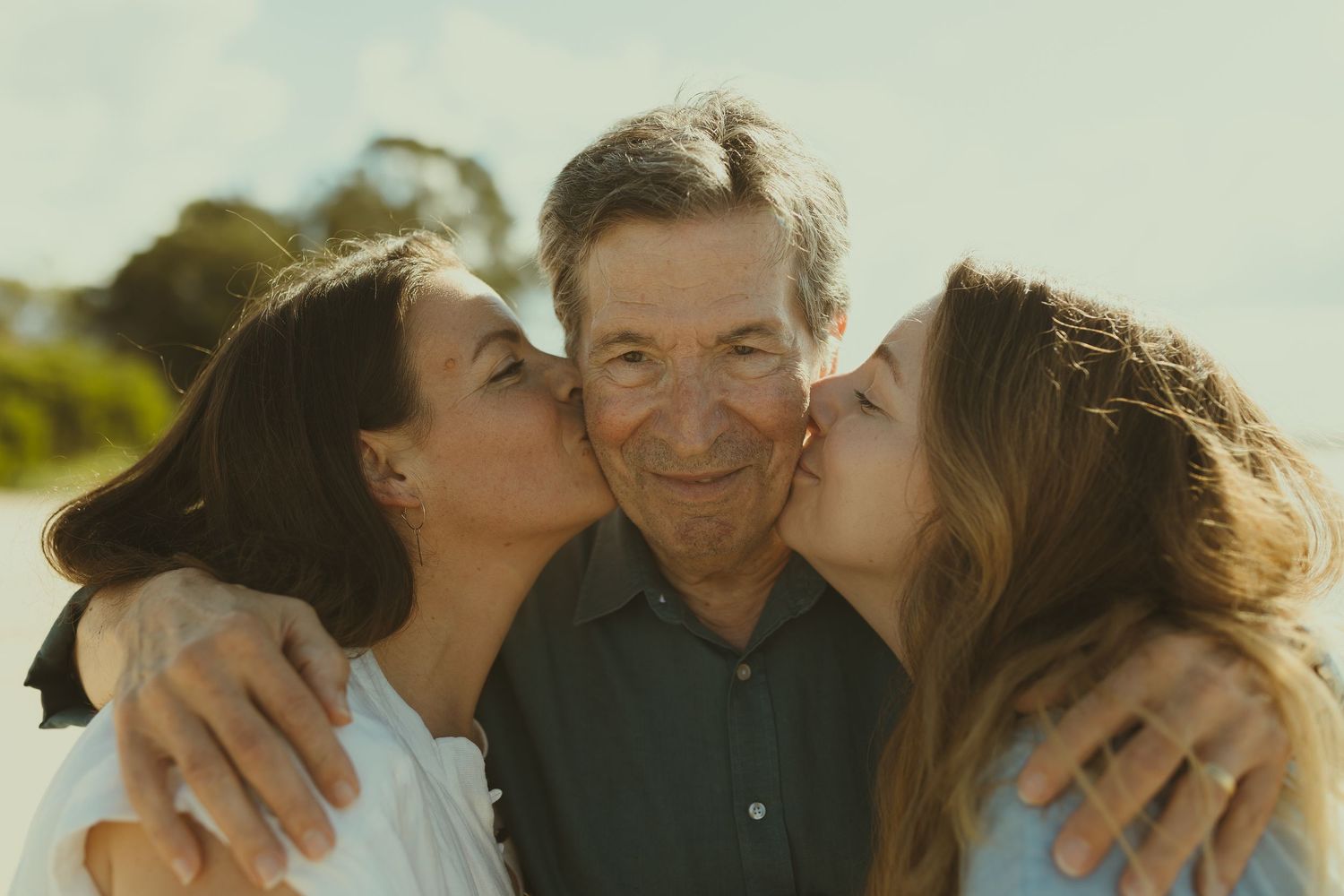 A group of people embrace and share joyful moments together outdoors in warm sunlight.