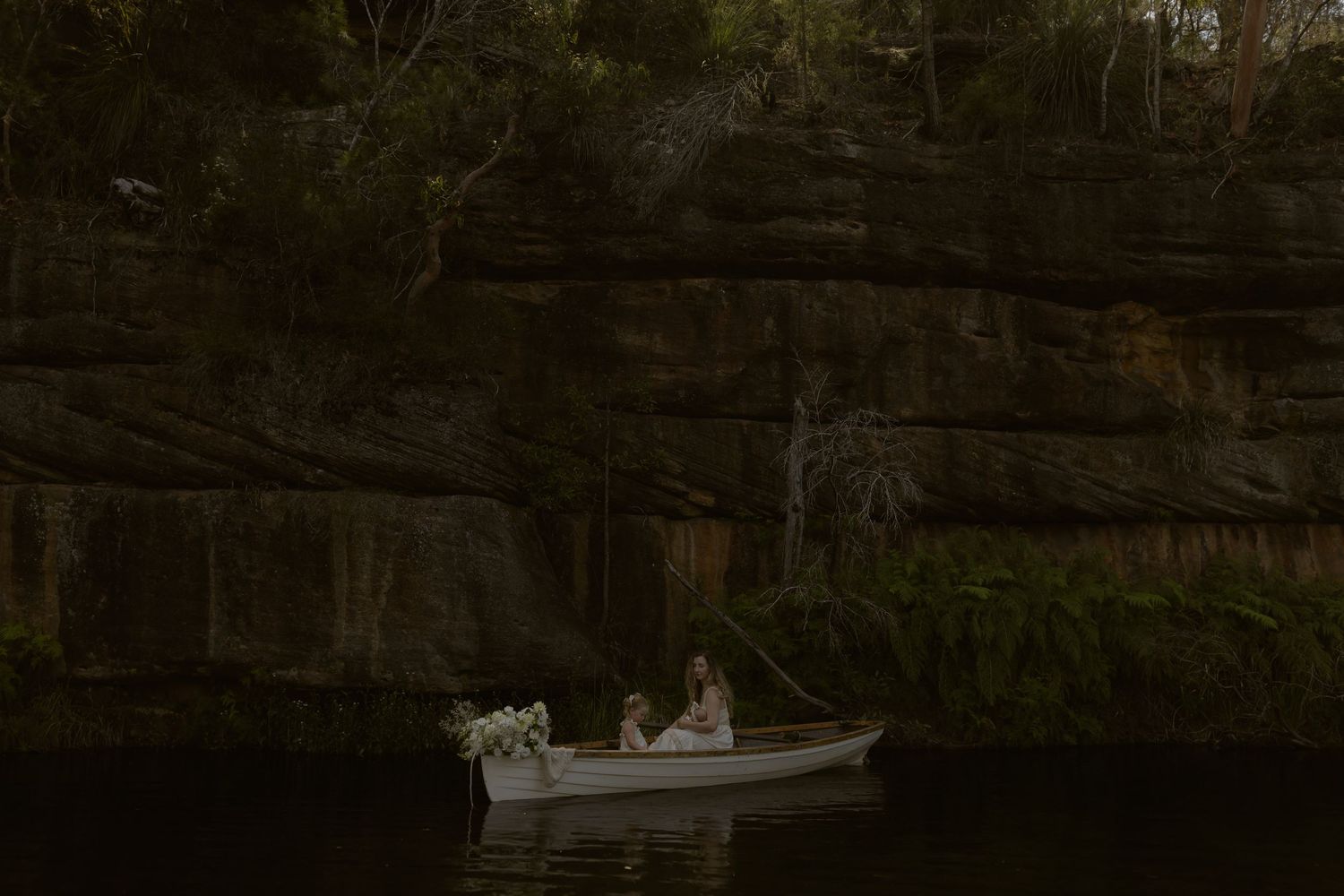 A serene lake surrounded by dense forest reflects the dark trees and sky in its calm waters at dusk.