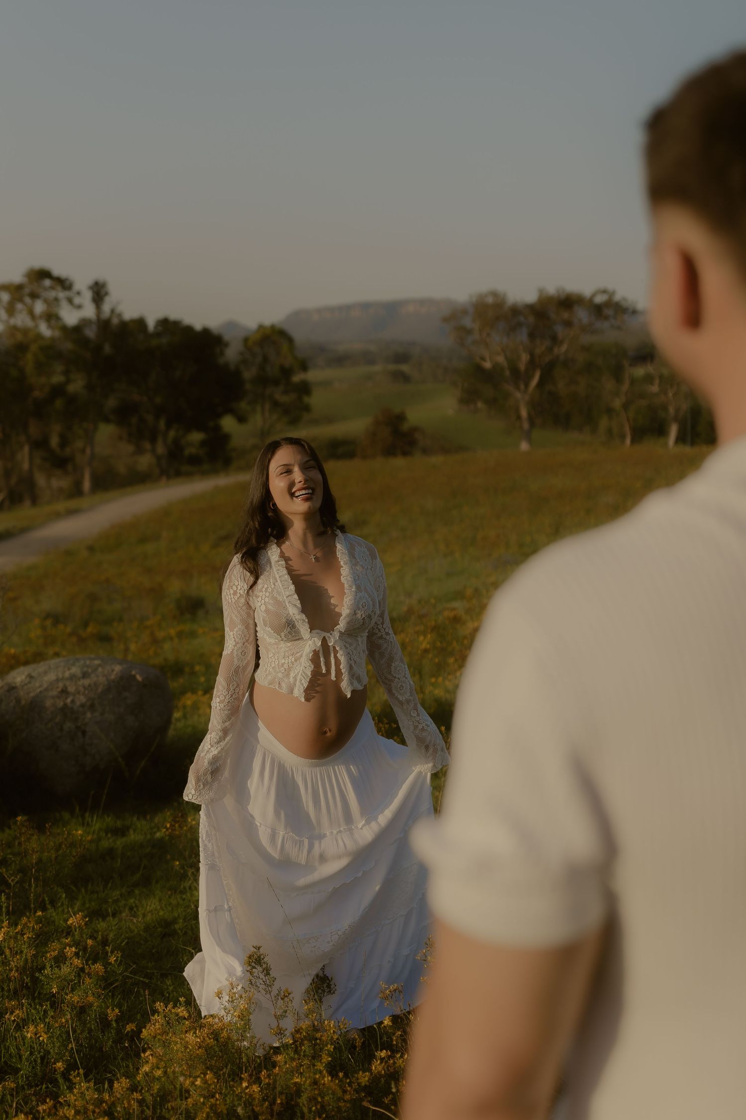 A person in a flowing white dress twirls joyfully in a sunlit meadow during golden hour.