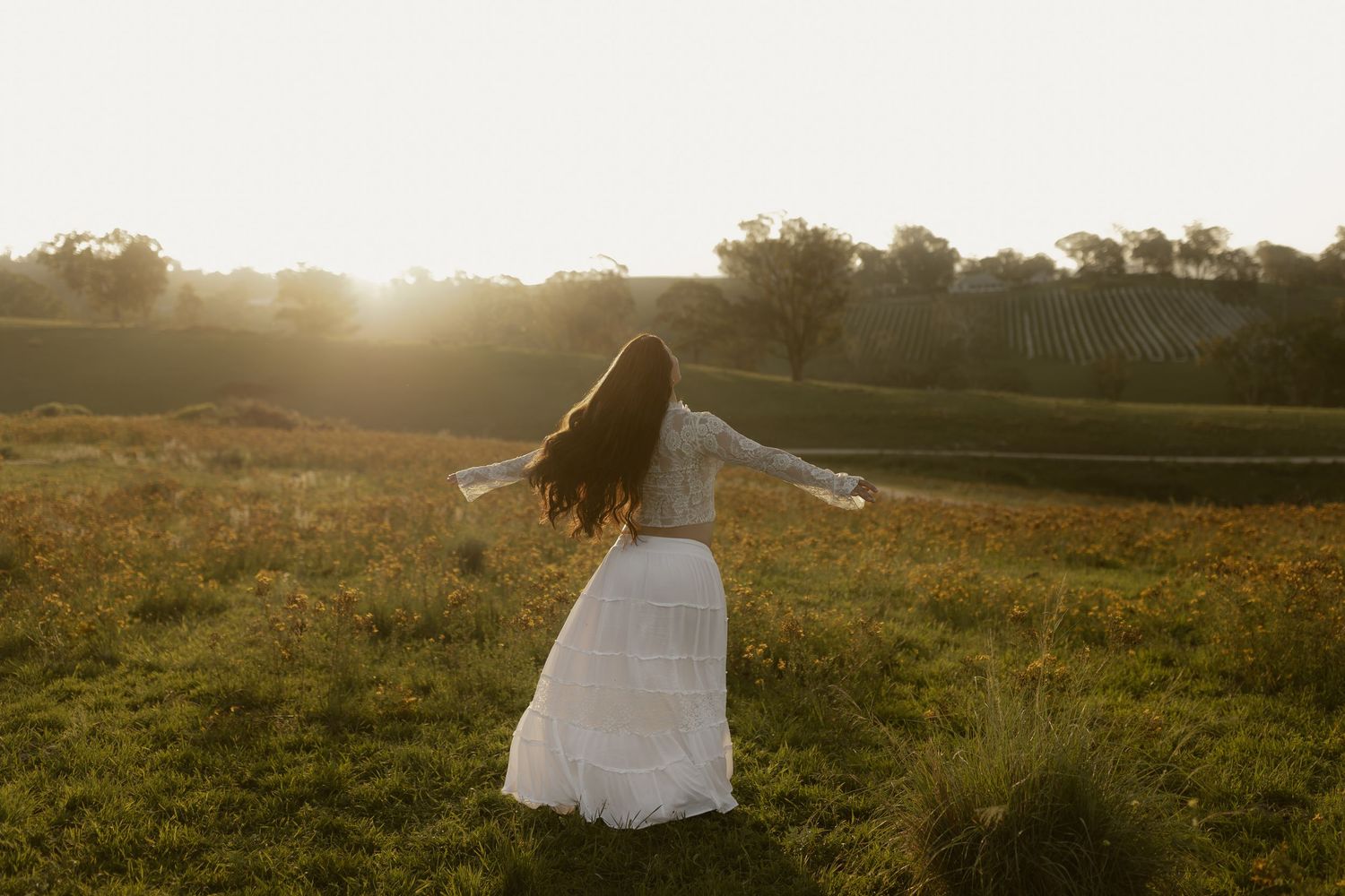 A person in a flowing white dress twirls joyfully in a sun-drenched meadow at golden hour.