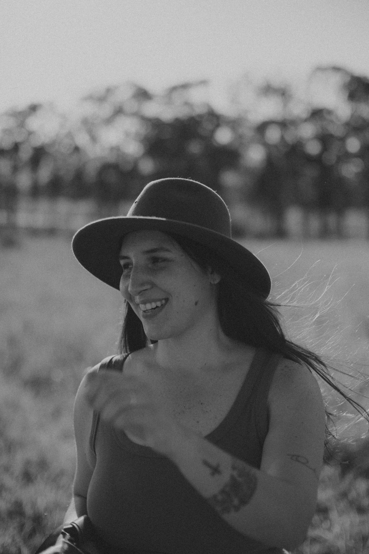 Black and white portrait series of a person in a wide-brimmed hat smiling and looking off into the distance.