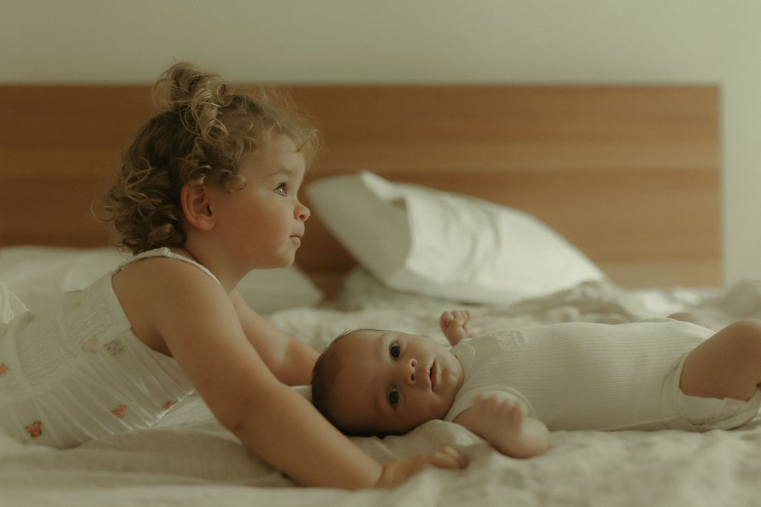 Two children sharing a sweet moment together while lying on white bedding in warm sunlight.