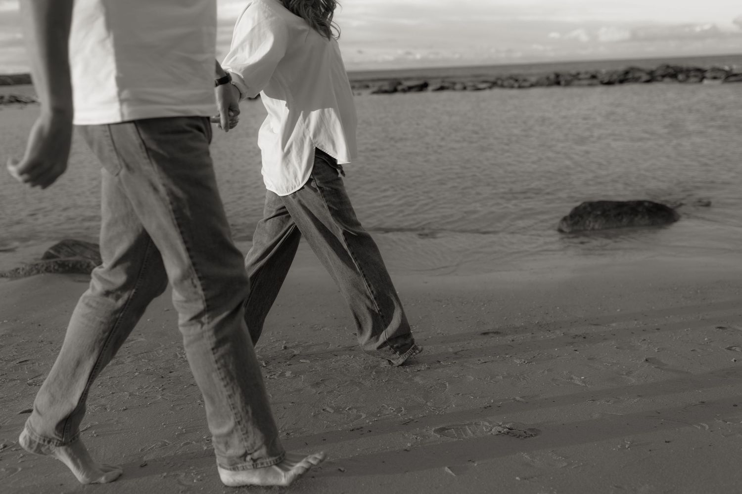 Two people walking barefoot on a sandy beach in black and white photo.
