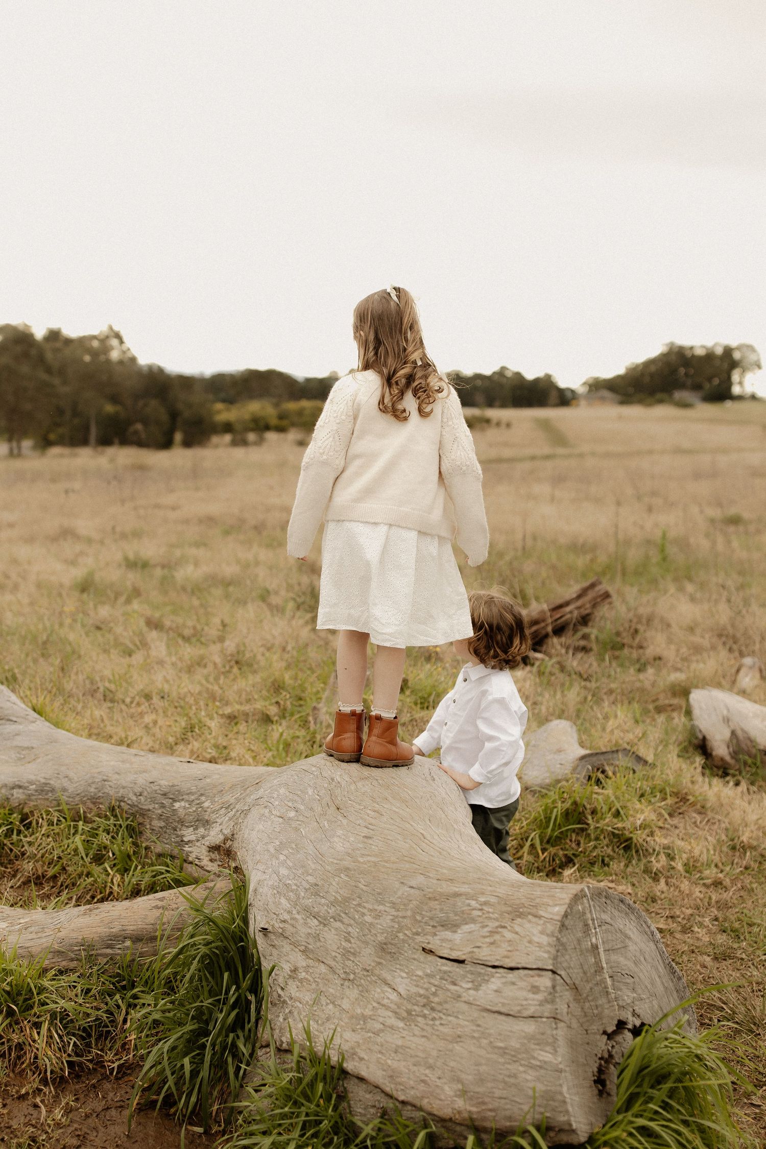A family in white attire sits together on a large rock in a serene field during golden hour.