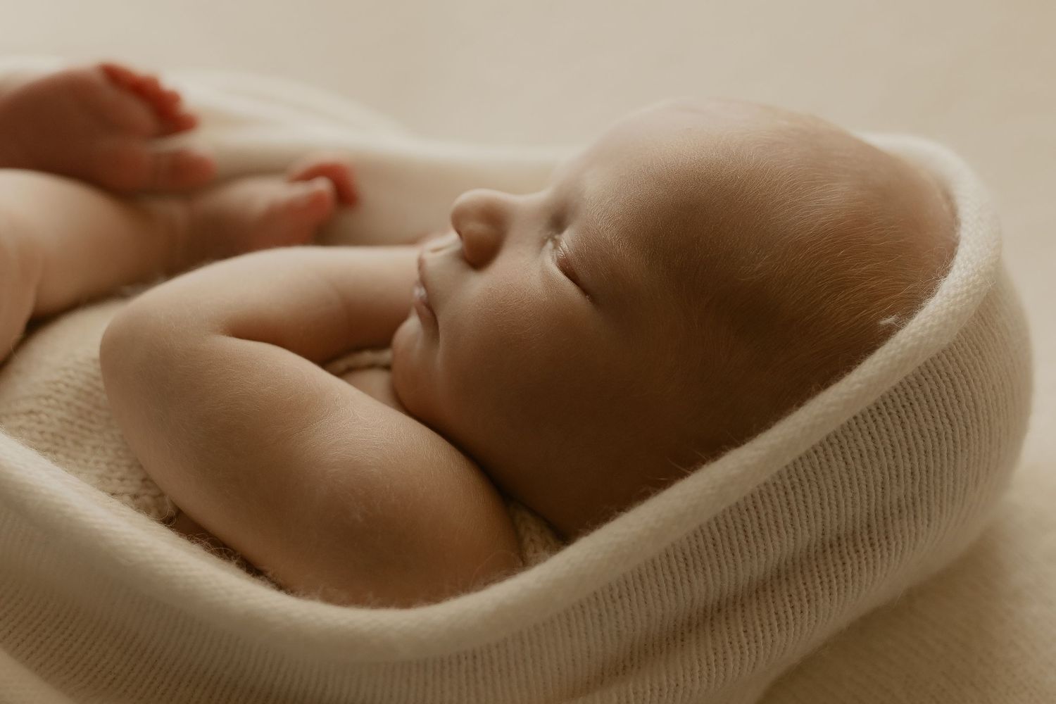 Sleeping baby bundled in a white blanket rests peacefully against a neutral beige background.