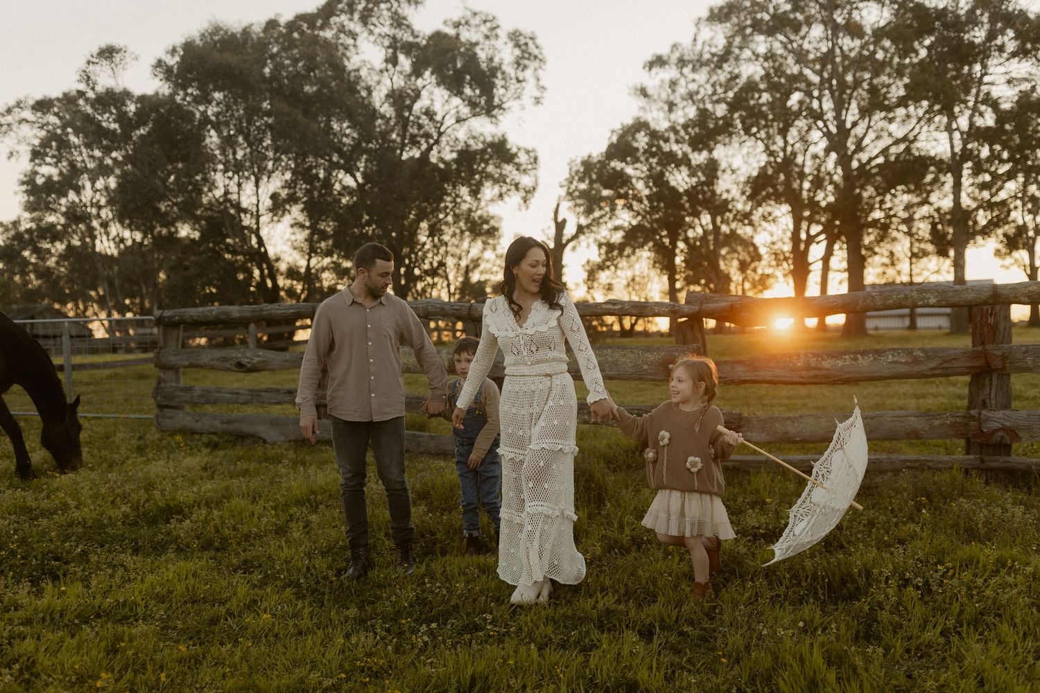 Family in white outfits stands together in a rustic field during golden hour sunset lighting.